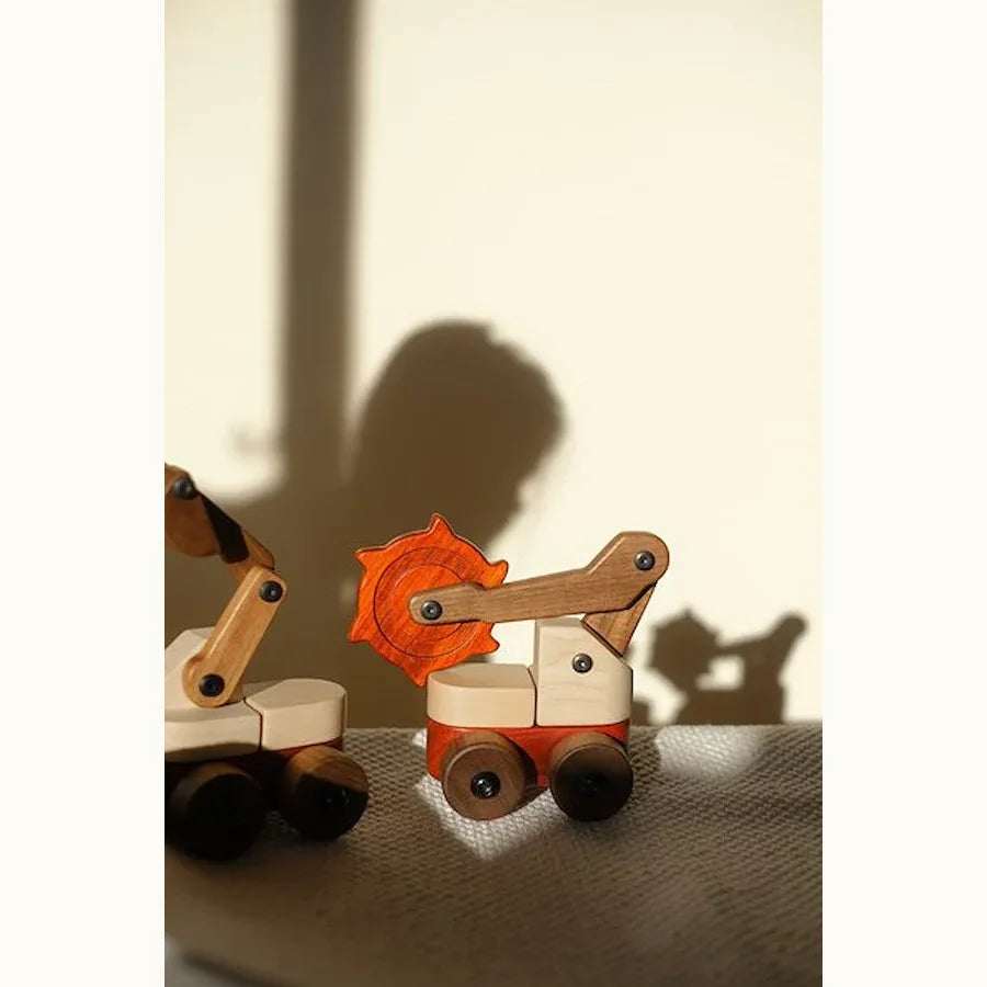 Two Padauk & Maple Trench Digger toys on linen, coral-red Padauk cutter wheel and Walnut details casting dramatic wall