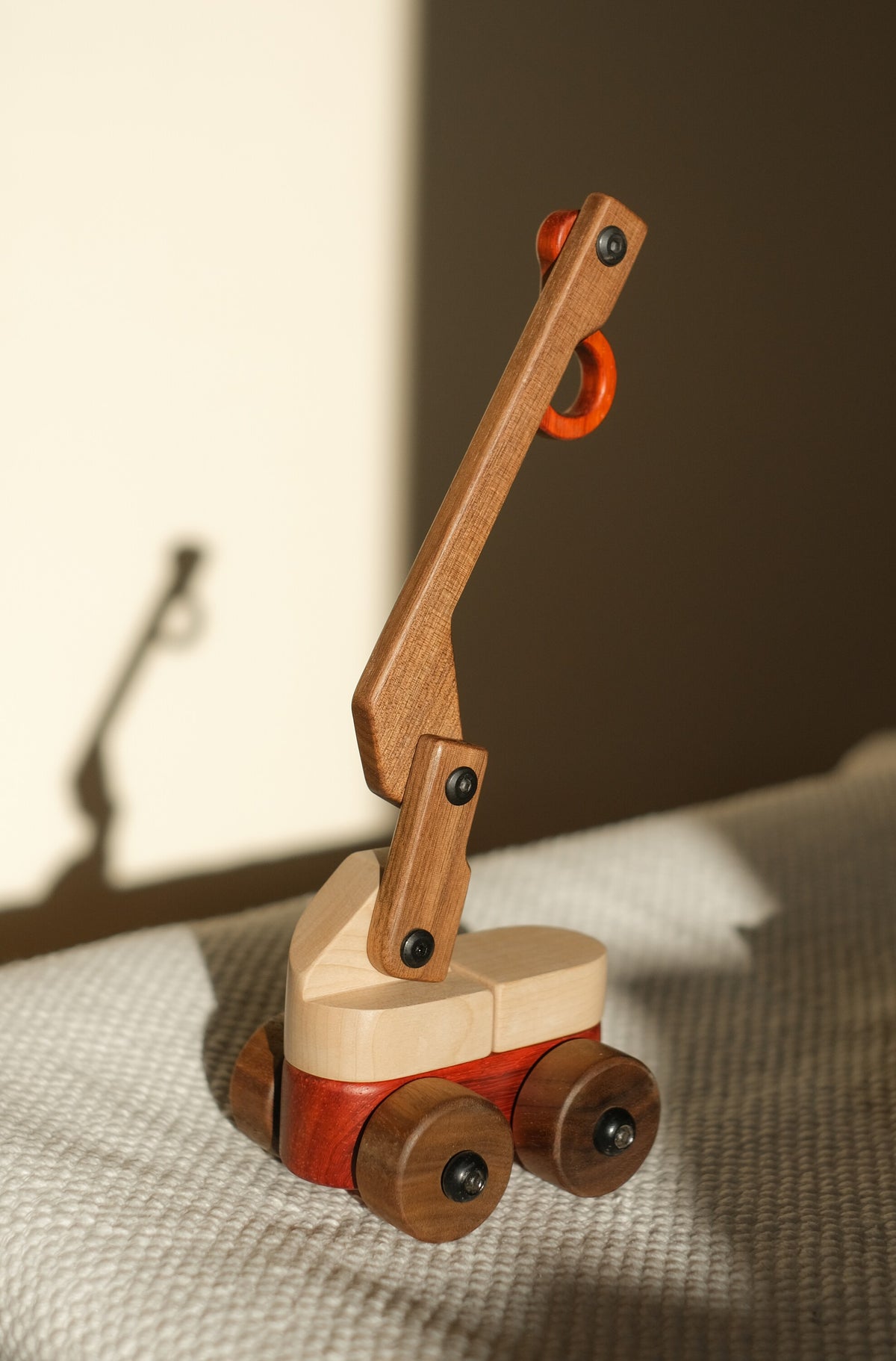 Walnut & Maple Crane with its jib raised on a grey textured throw, in warm window light with its shadow on the wall