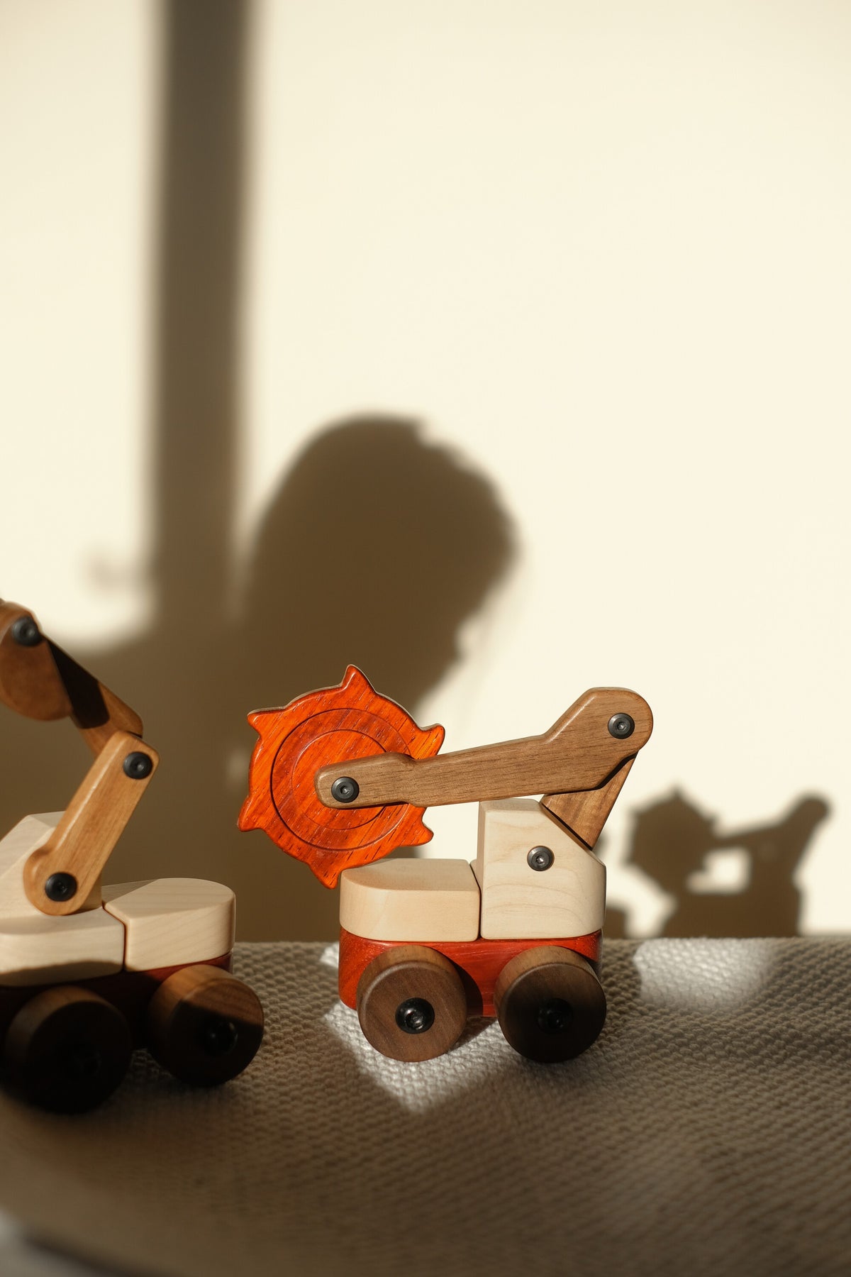 Padauk & Maple Trench Digger and the Maple & Padauk Excavator on a woven throw, a child's shadow on the sunlit wall behind