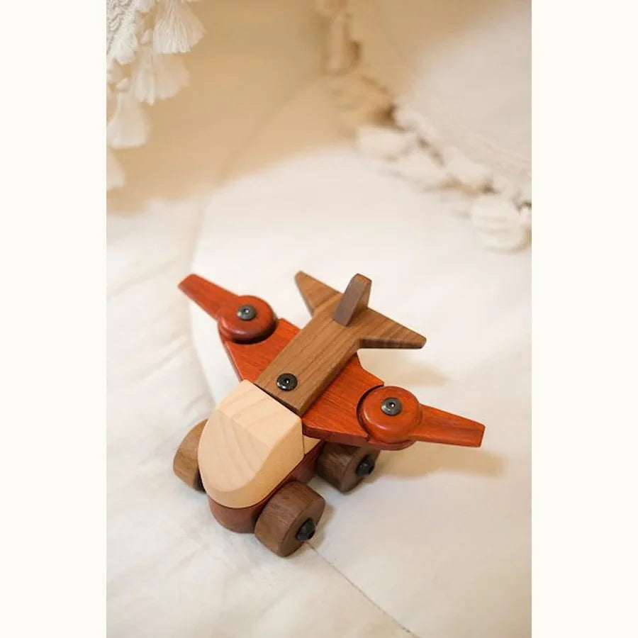 Walnut & Padauk Aeroplane overhead lifestyle shot on cream linen, showing coral padauk wings, dark walnut tail, and pale