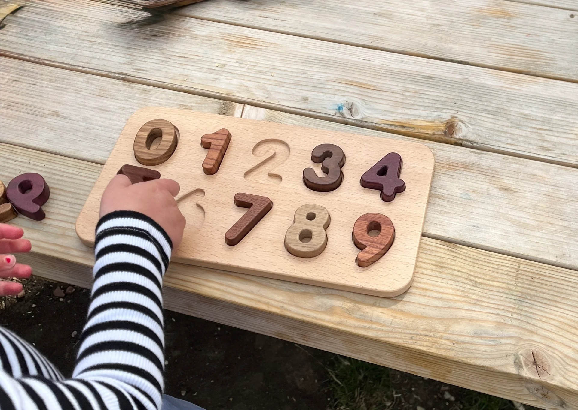 Wooden number puzzle on a wooden surface with a child's hand reaching for it.