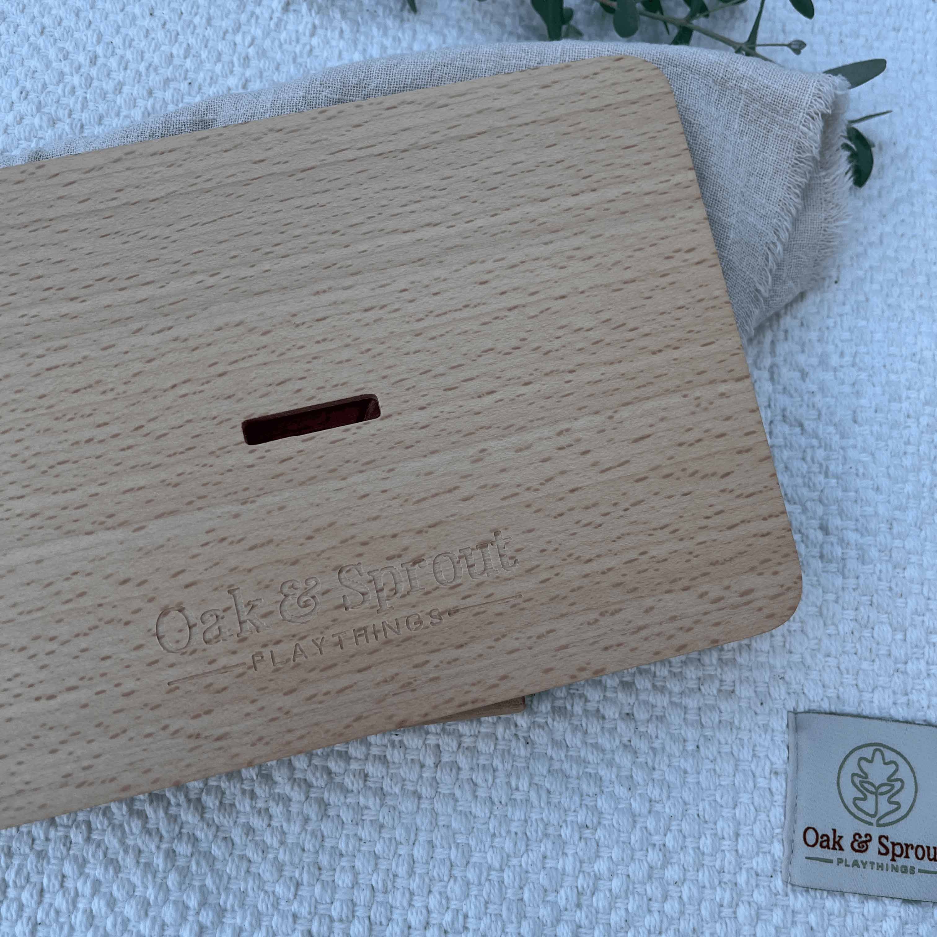 Sky Bloom puzzle beech board back showing debossed Oak & Sprout logo, finger-pull slot, and branded fabric label on white pla