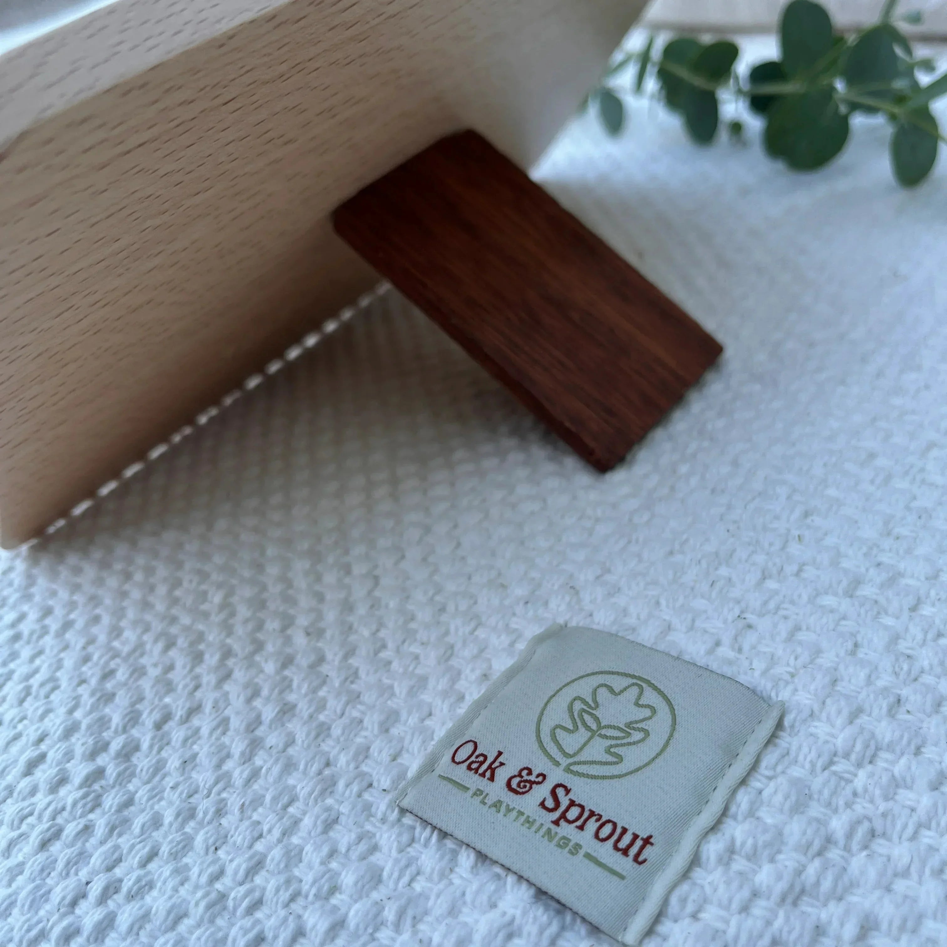 Sky Bloom puzzle back showing beech frame and walnut piece, Oak & Sprout label on white cotton playmat with eucalyptus