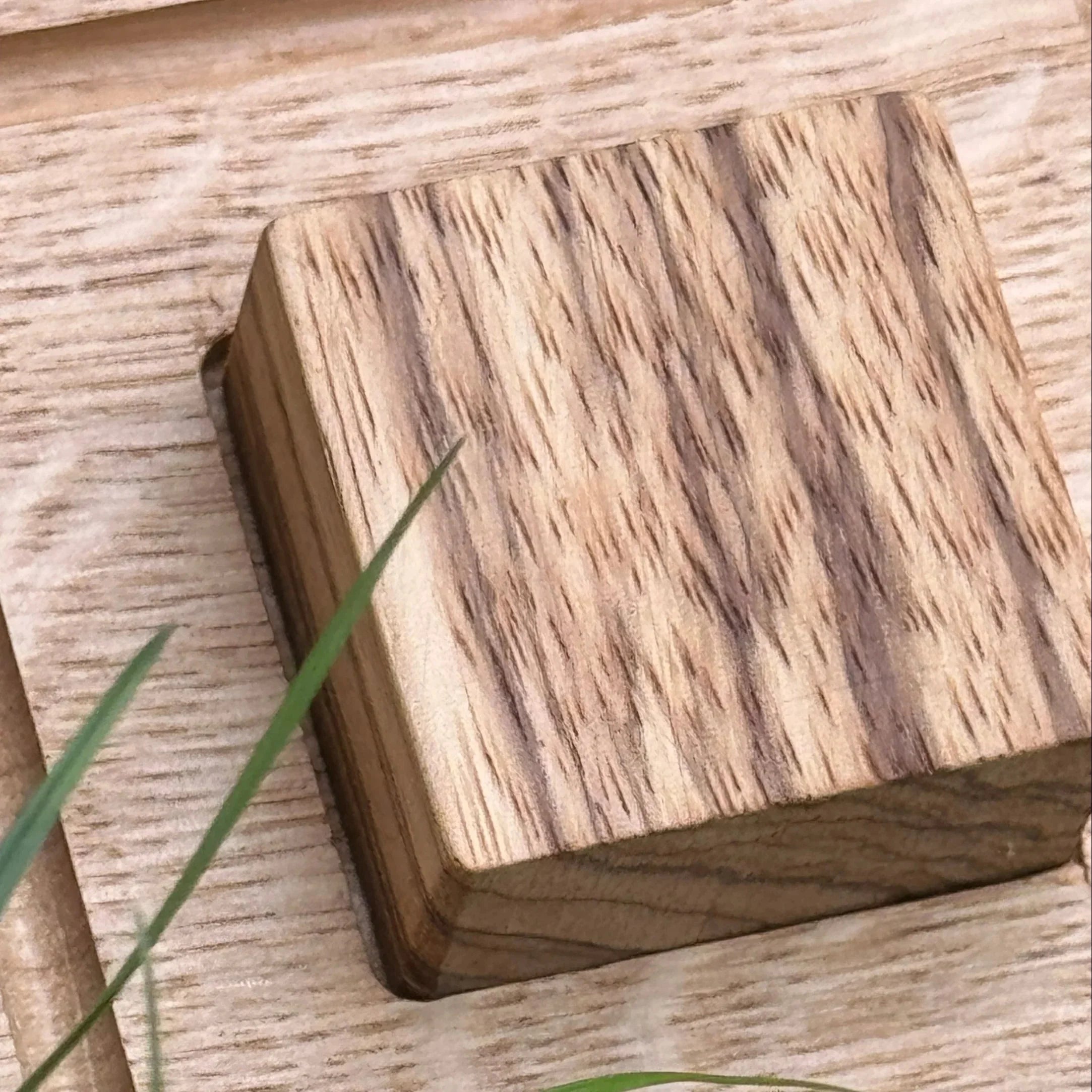 Trace & Place Zebrano shape piece showing bold striped grain, resting on limed oak surface with grass blades