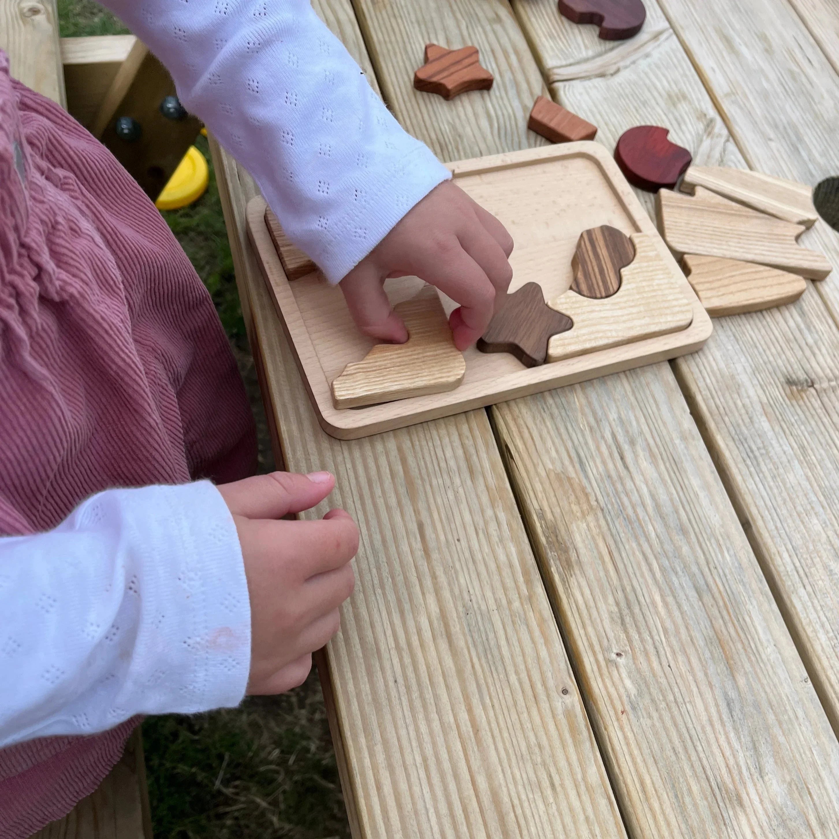 Child playing with Sweet Scoops puzzle outdoors, walnut and padauk pieces scattered on weathered decking table