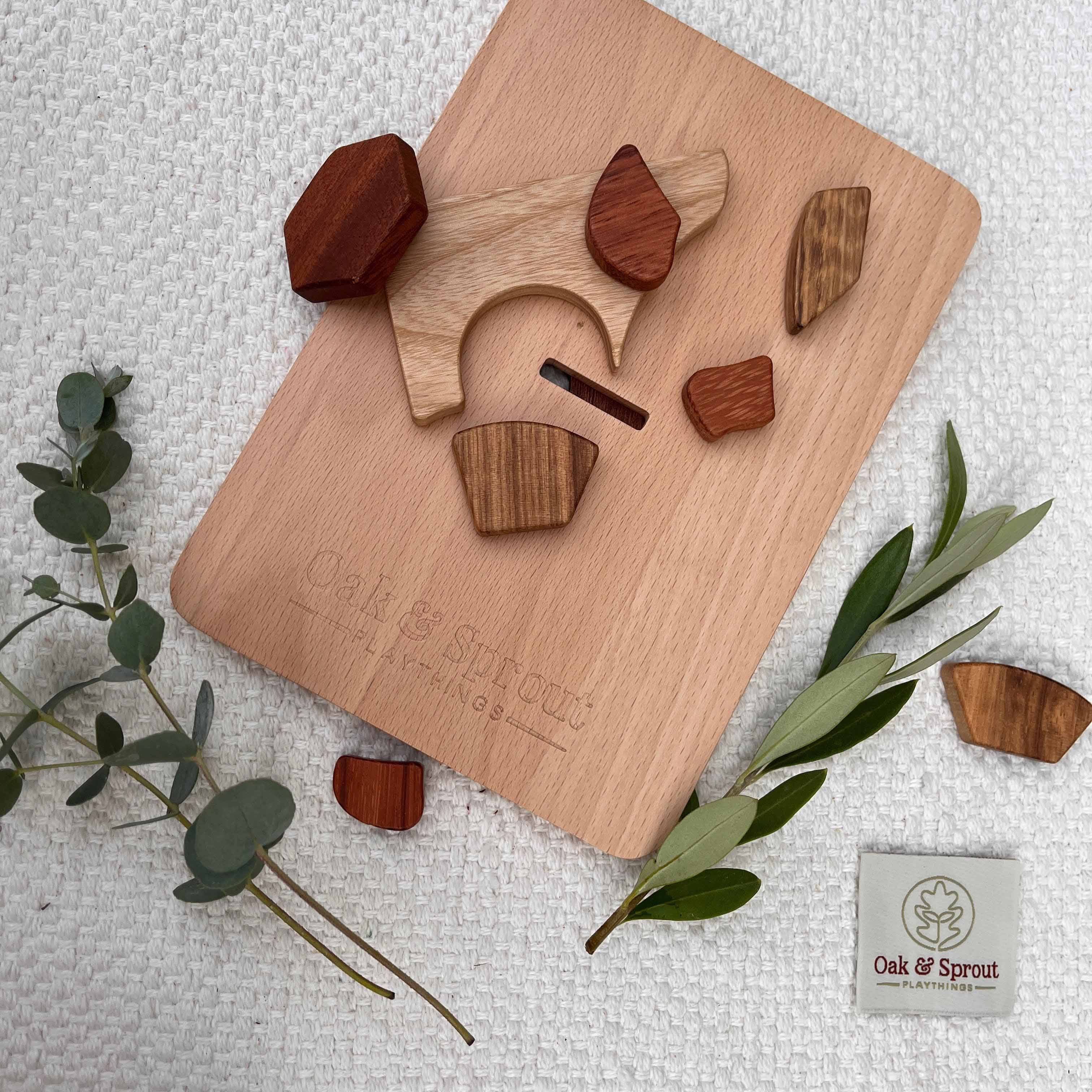 Sweet Scoops puzzle disassembled, Padauk and Tigerwood pieces scattered around engraved Oak & Sprout board on linen