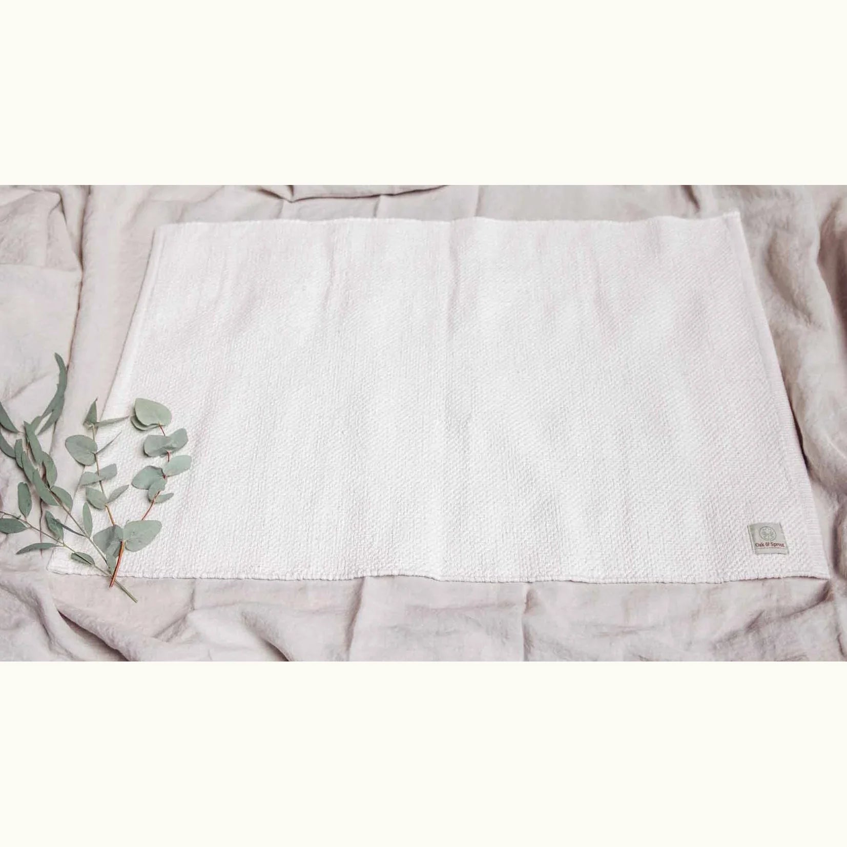Oak & Sprout Playmat laid flat on neutral linen, showing full cream woven textile with branded label and eucalyptus sprig