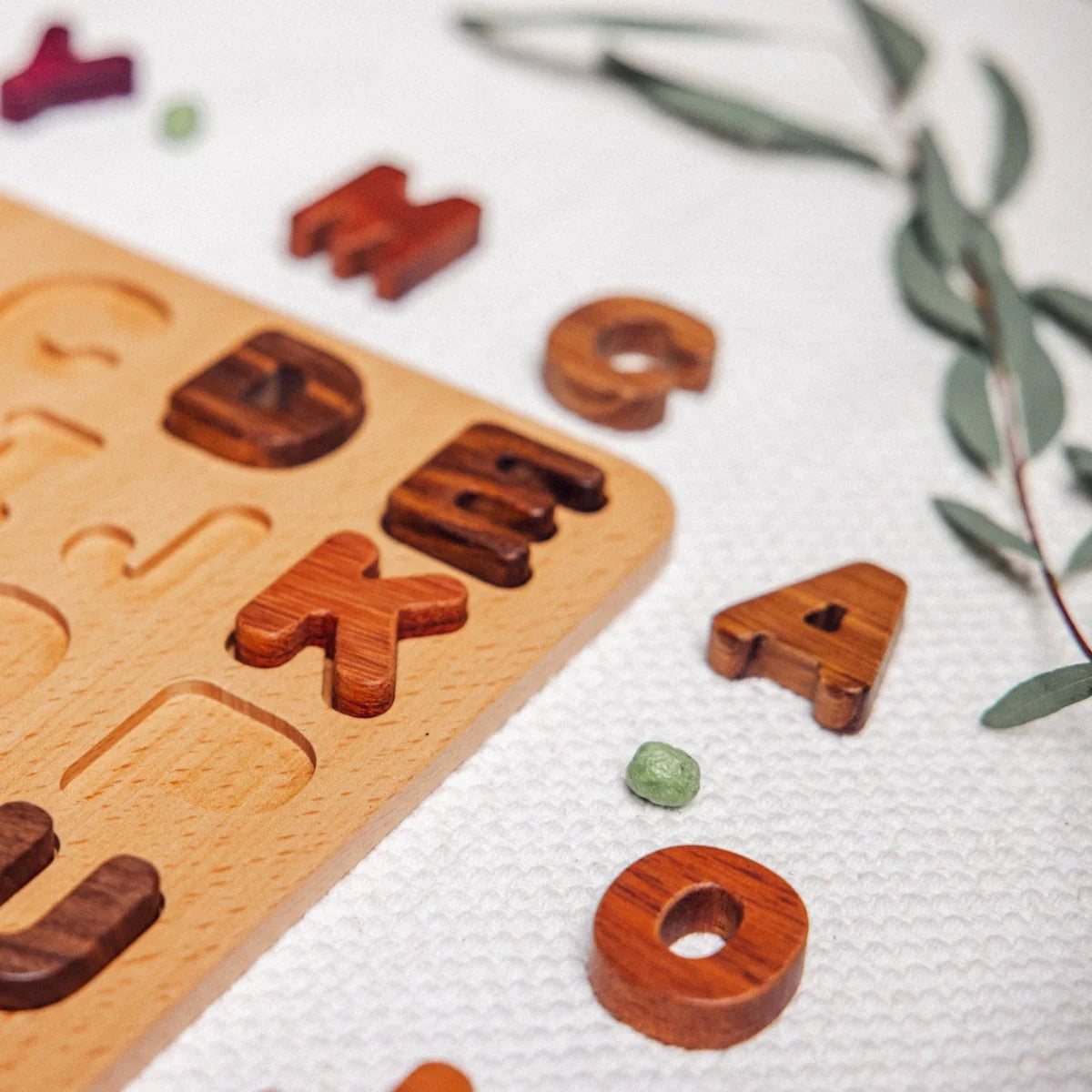Oak & Sprout uppercase alphabet puzzle partially assembled, tigerwood, walnut and mahogany letter pieces scattered on linen m