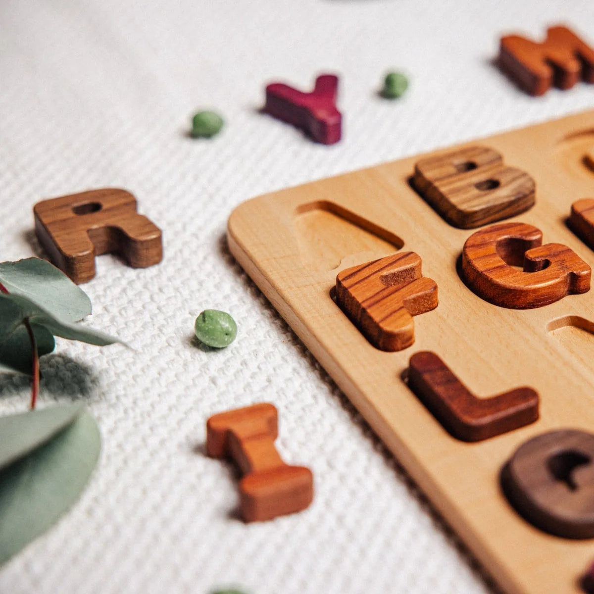 Oak & Sprout Alphabet Puzzle partially assembled on muslin playmat, with loose Walnut, Tigerwood and Purpleheart letter piece