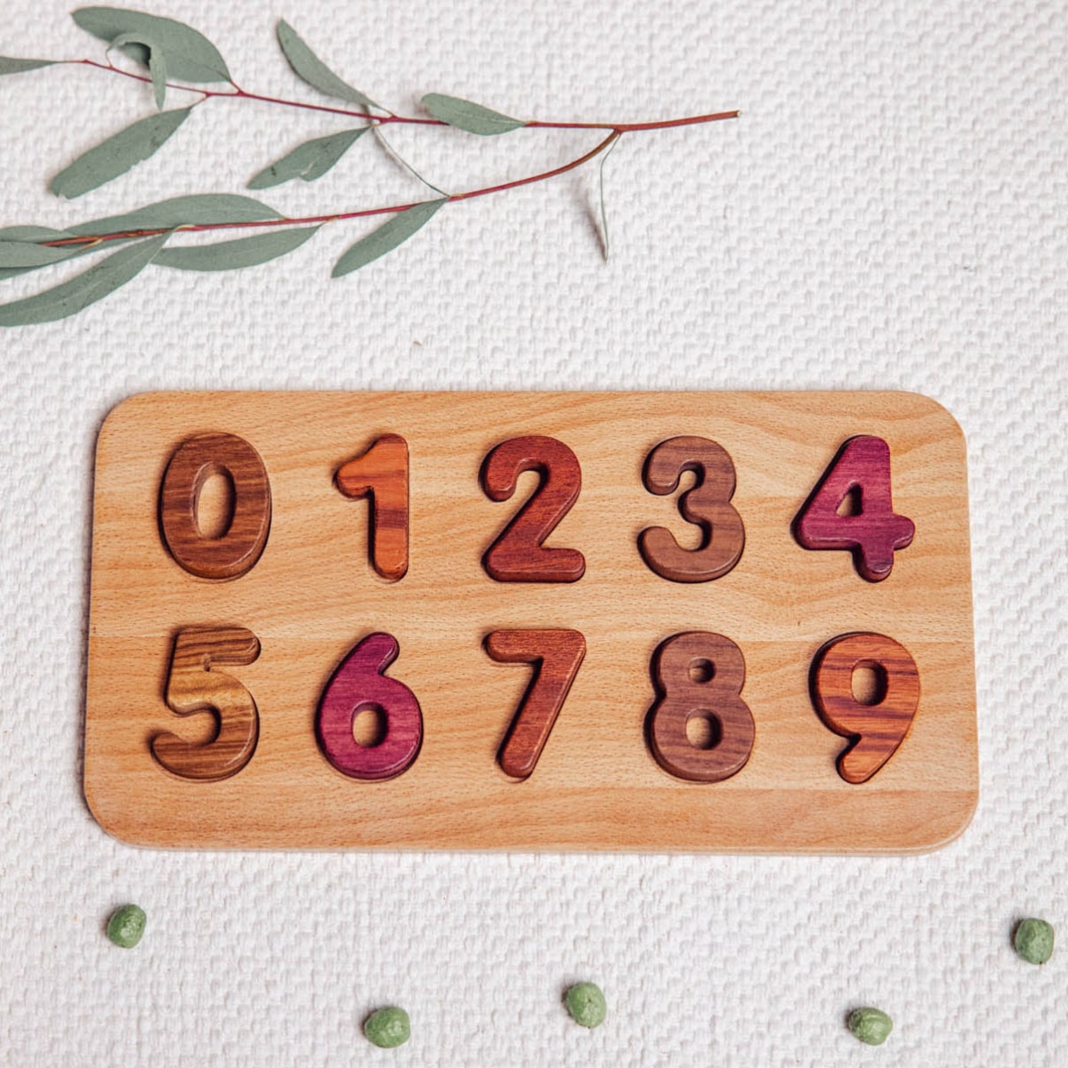 Oak & Sprout number puzzle board 0–9, flat-lay on linen, pieces in Purpleheart, Tigerwood, Walnut and Mahogany tones