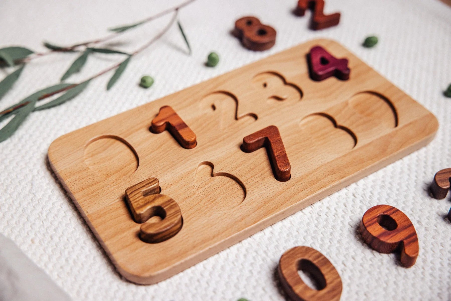 Wooden puzzle with numbers on a white surface with greenery