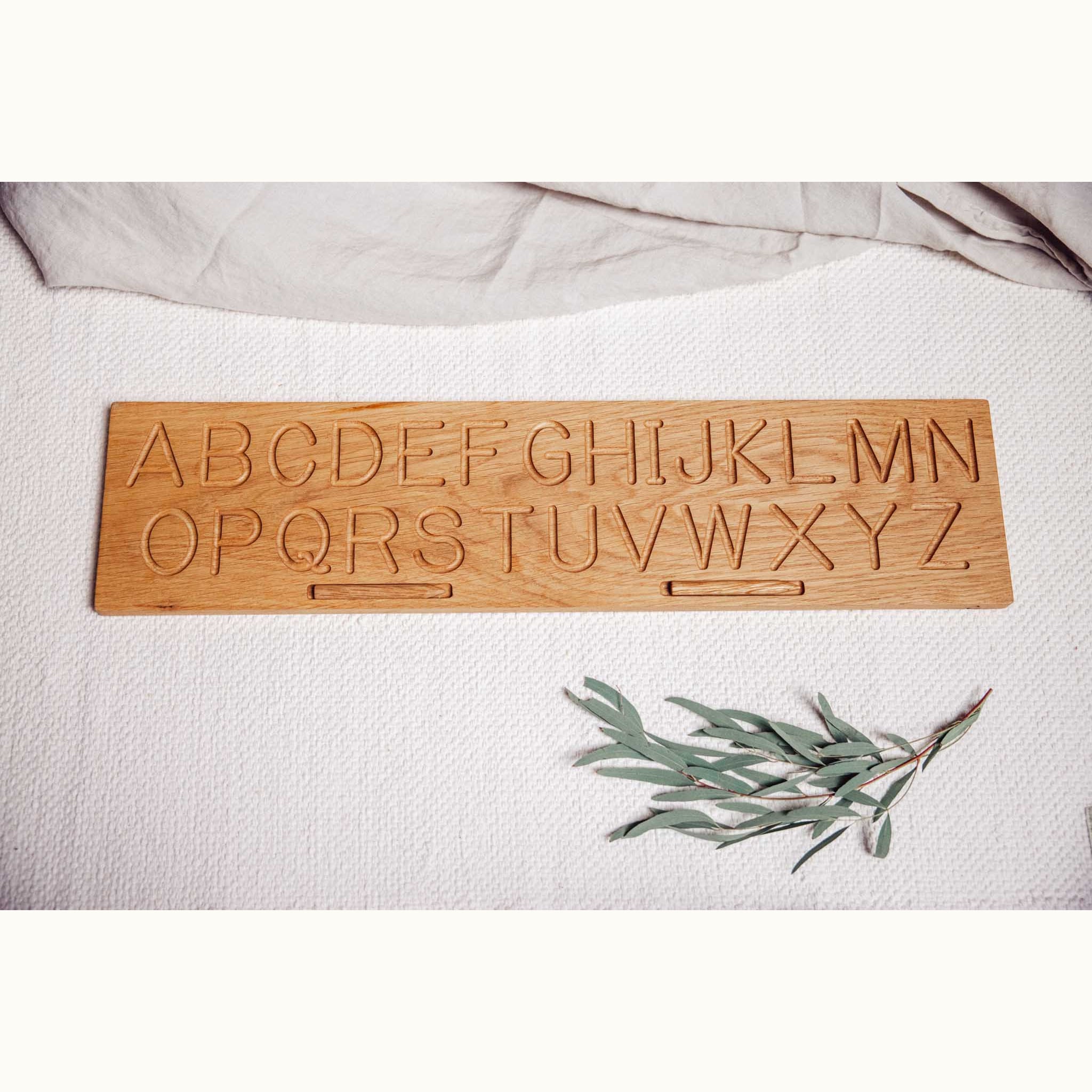 Oak alphabet tracing board face-up showing A–Z capital letters engraved in two rows, with natural honey-golden grain visible