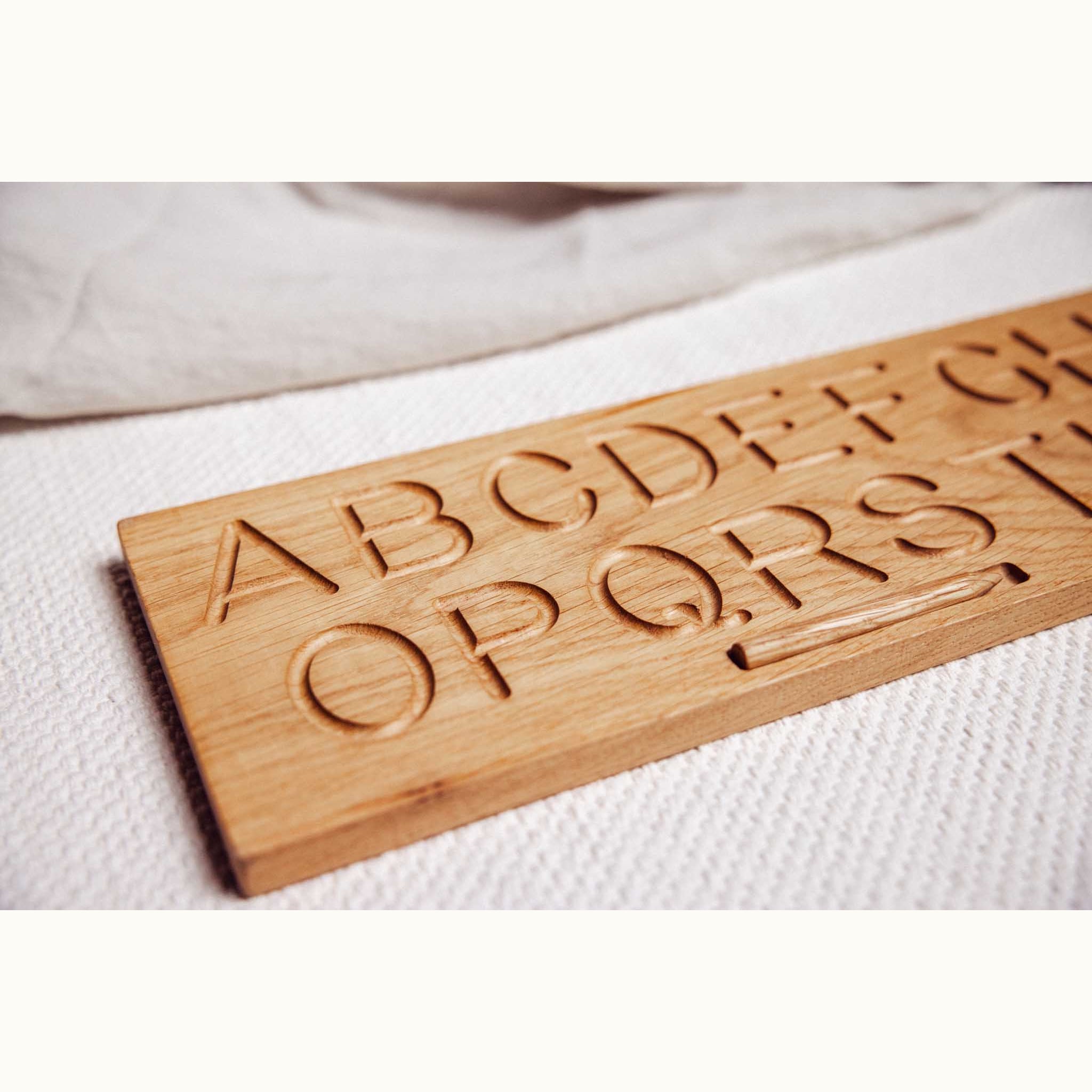 Close-up of oak Alphabet Tracing Board showing engraved capital letters A–Z routed into warm honey-toned solid oak grain