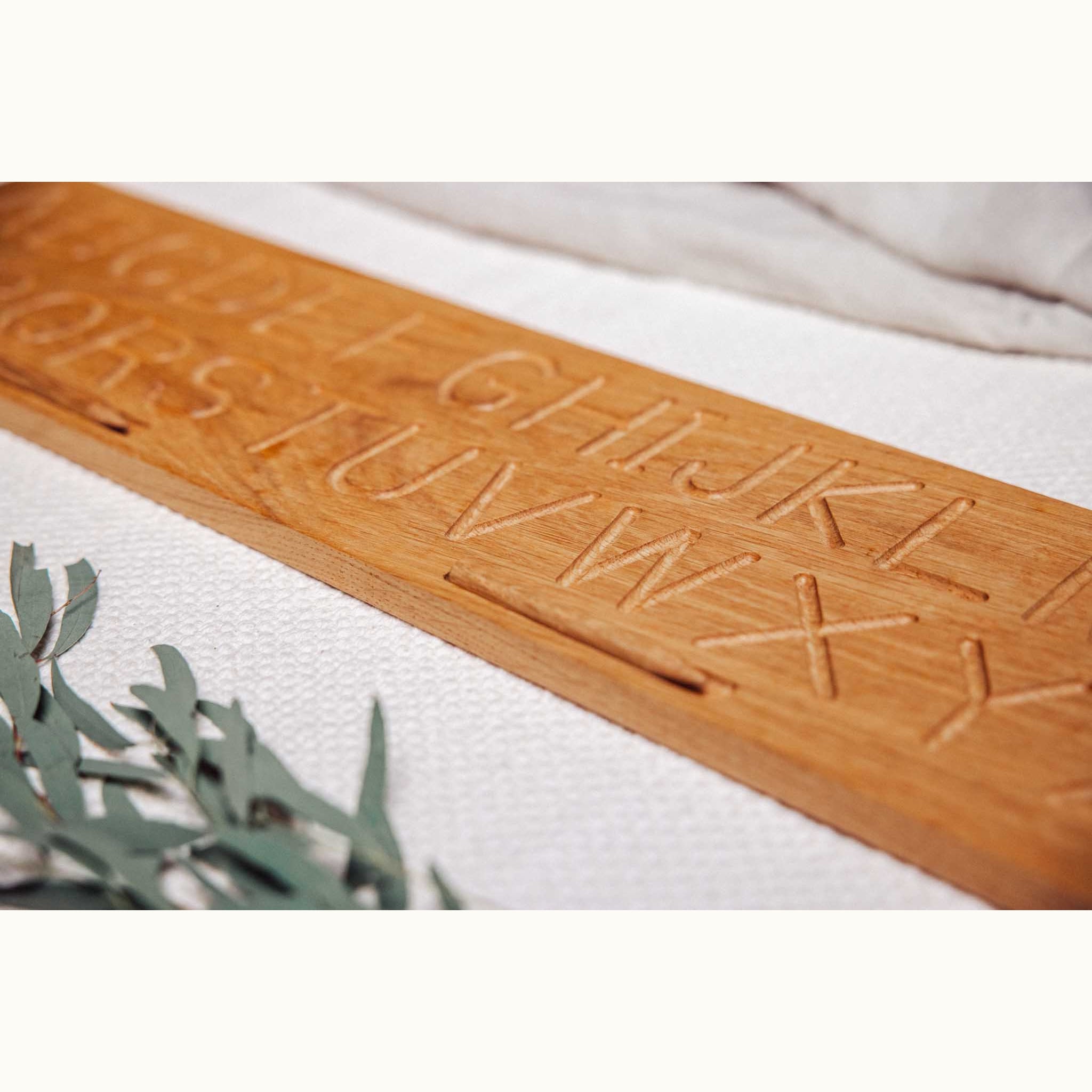 Oak alphabet tracing board flat lay, low-angle close-up showing hand-routed uppercase letter grooves G–Z in natural honey oak