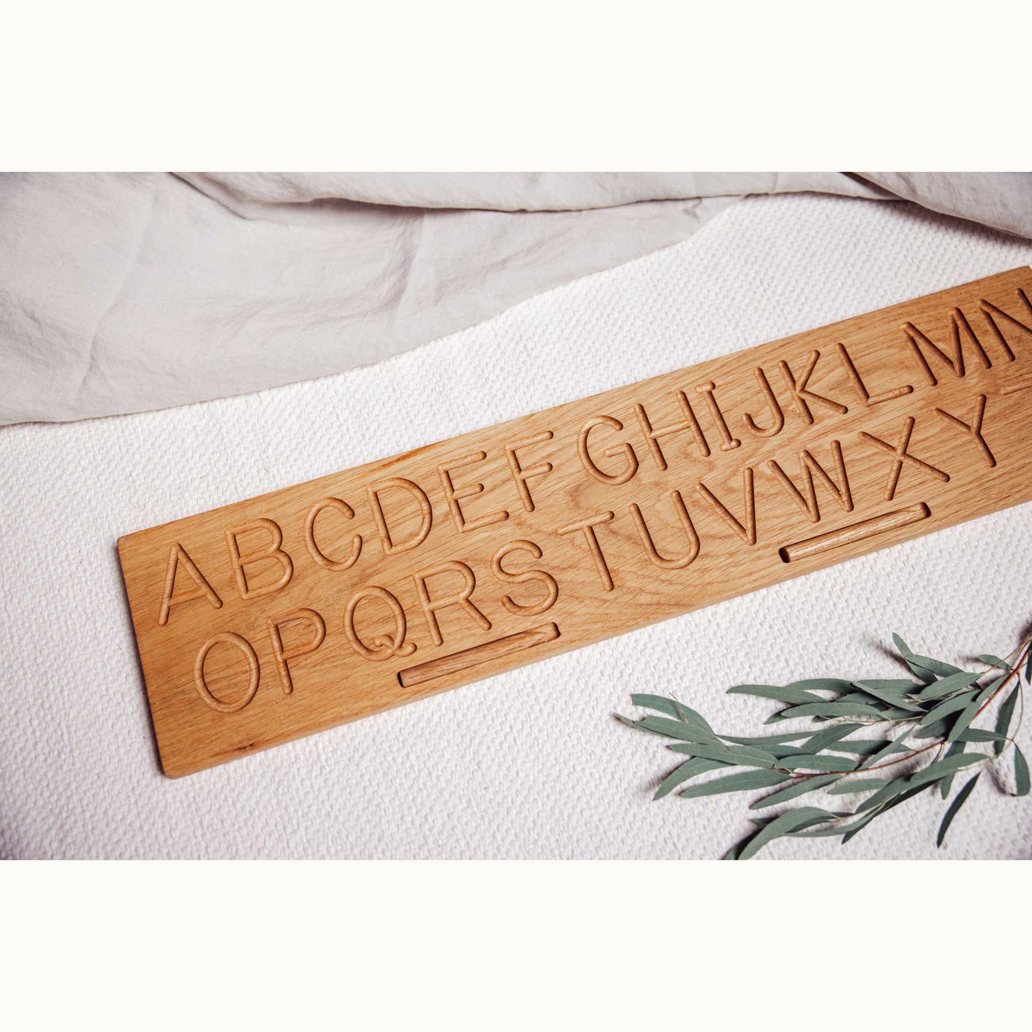 Oak alphabet tracing board laid flat showing full A–Z letters routed into warm honey-toned solid oak grain