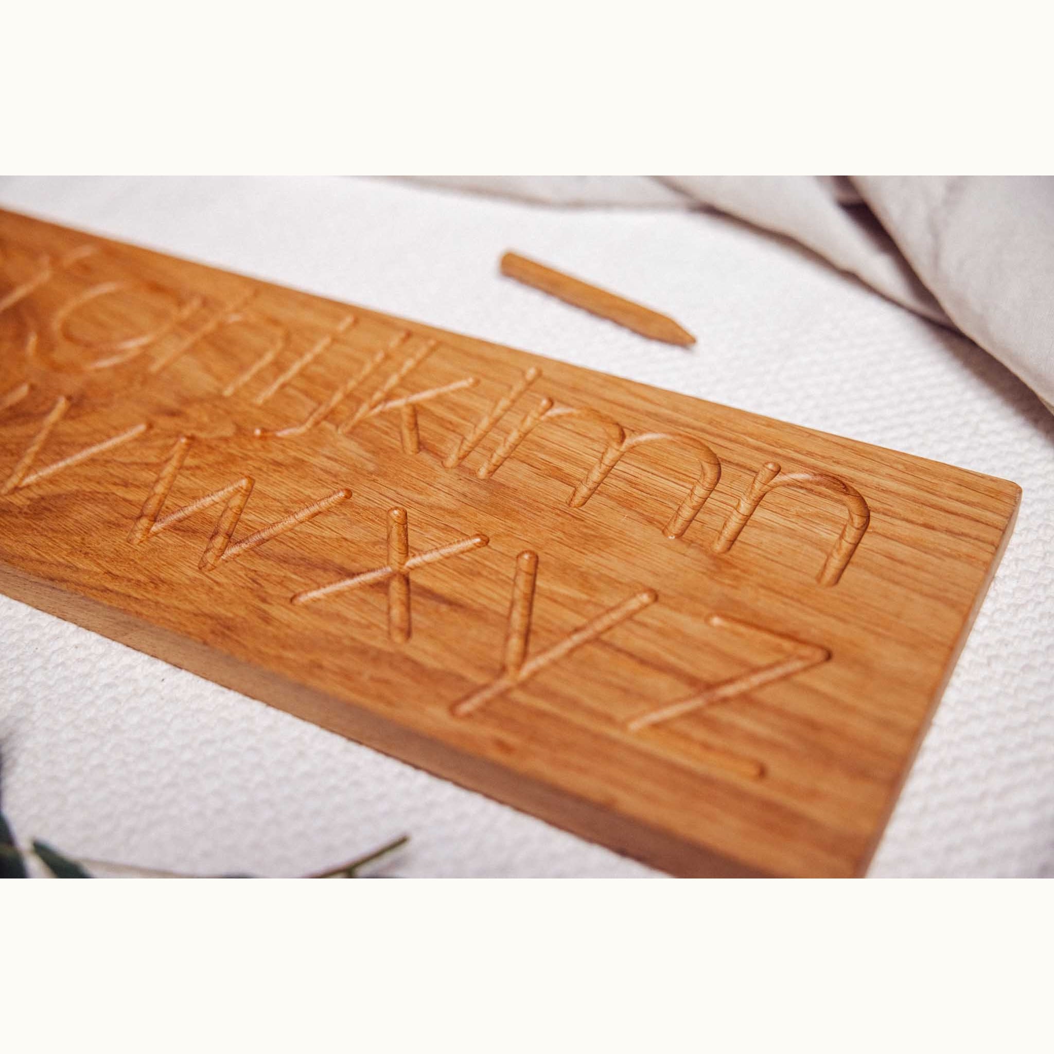 Close-up of oak Alphabet Tracing Board showing deeply engraved letters M–Z with wooden stylus on textured playmat
