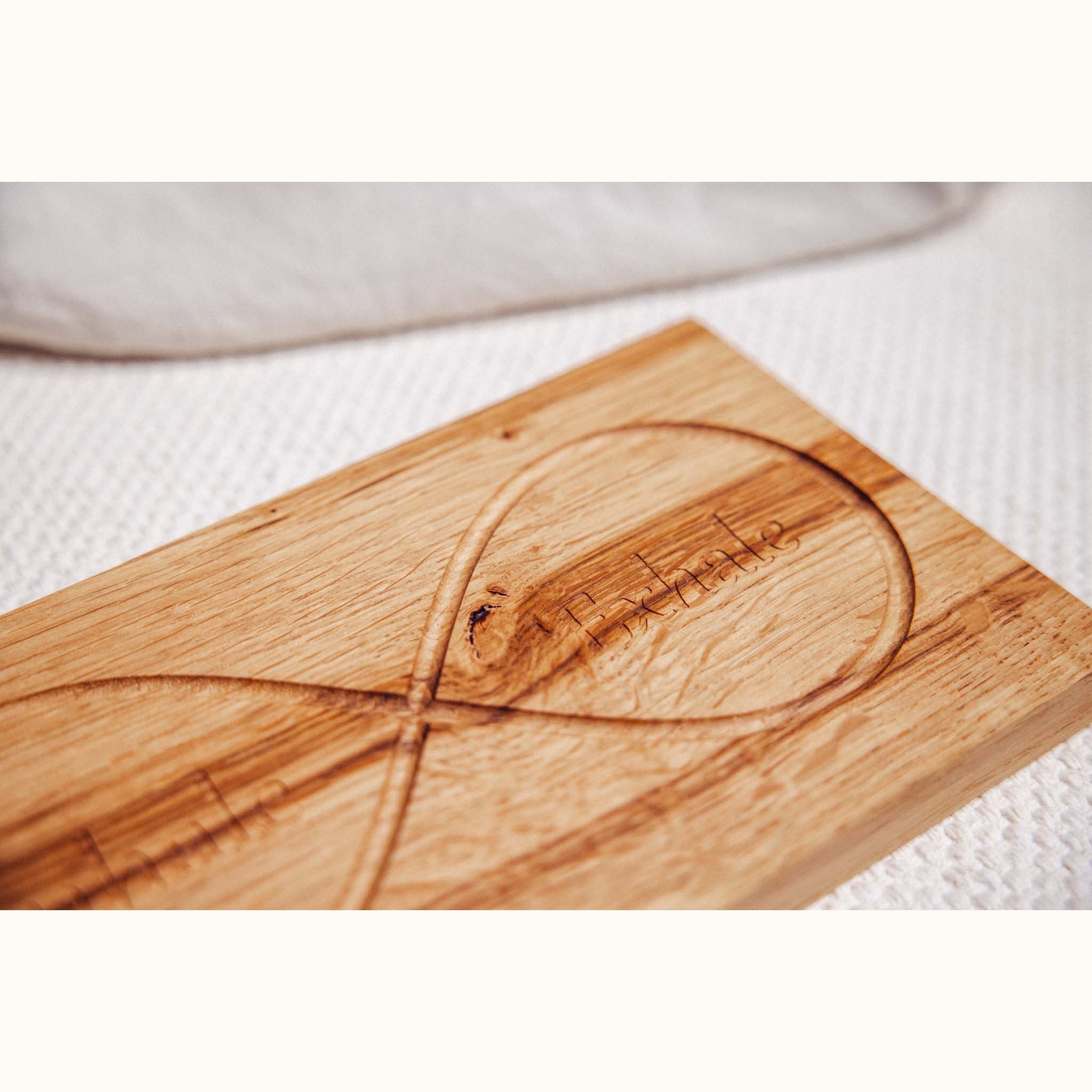 Infinity Breathing Board in oak, close-up of engraved infinity loop and 'Exhale' text, natural grain and knot visible