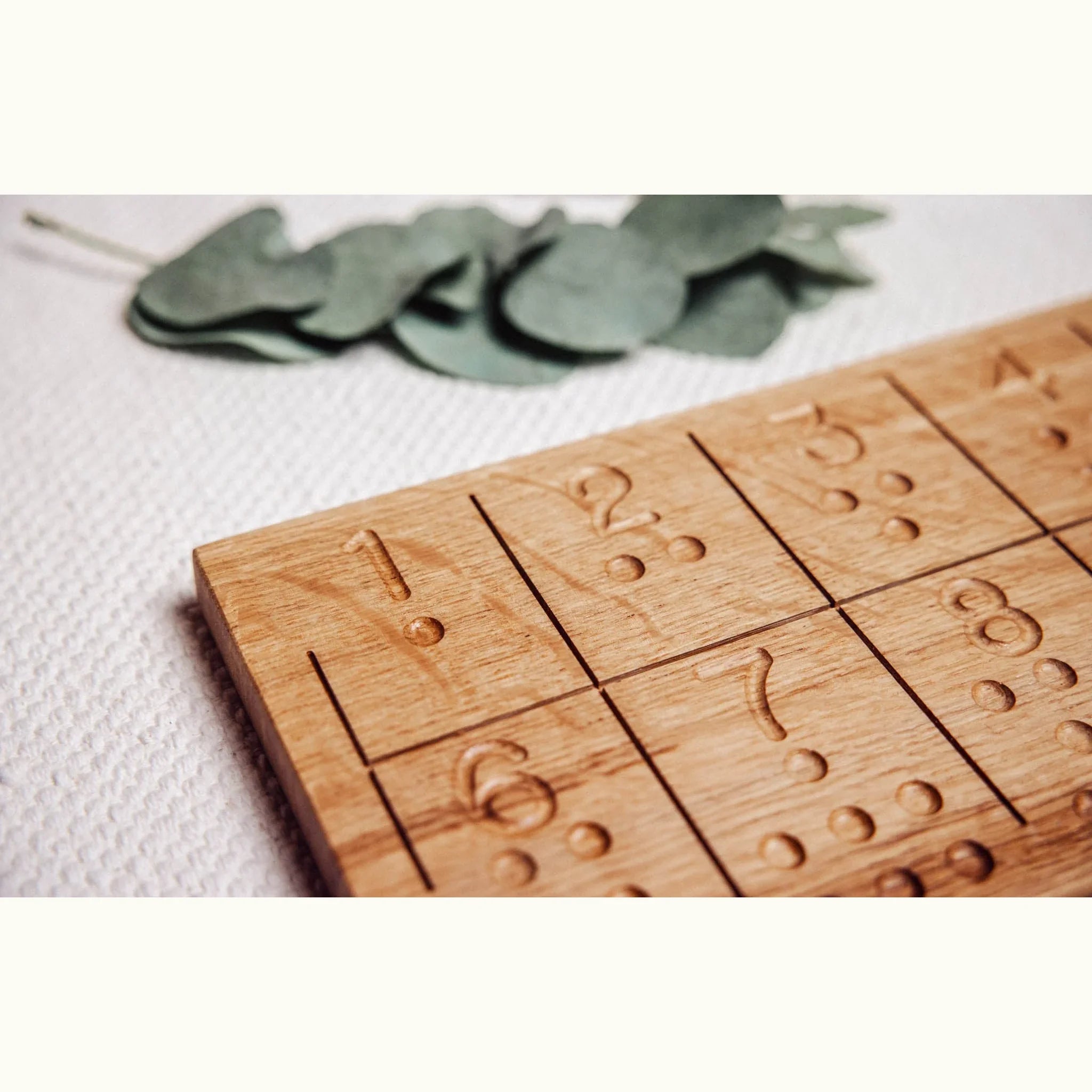 Numbers Tracing & Balls oak board close-up showing hand-carved numerals and tactile dot indentations across grid cells