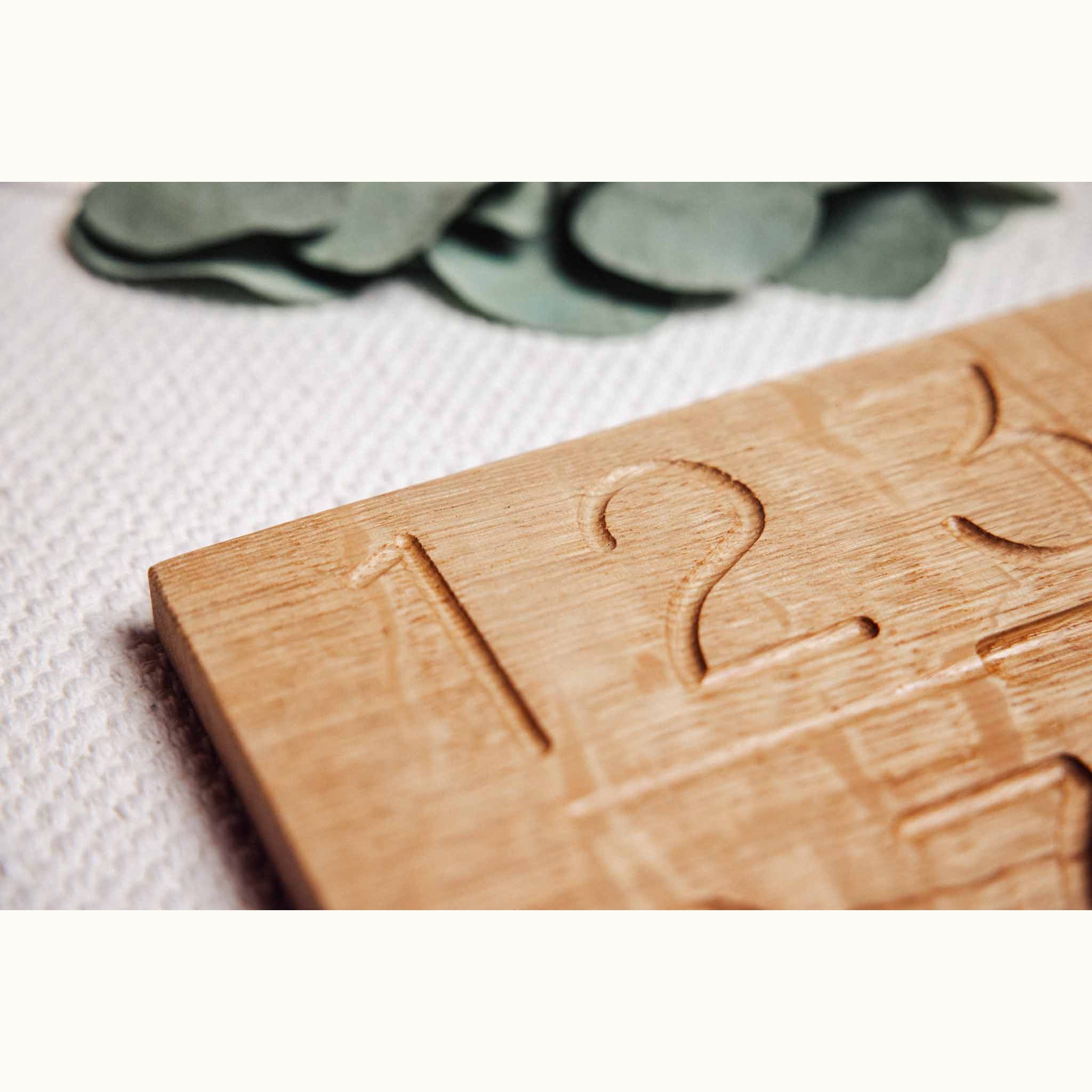 Numbers Tracing & Balls oak board close-up showing hand-carved numerals 1 and 2 with tactile tracing grooves in warm honey gr