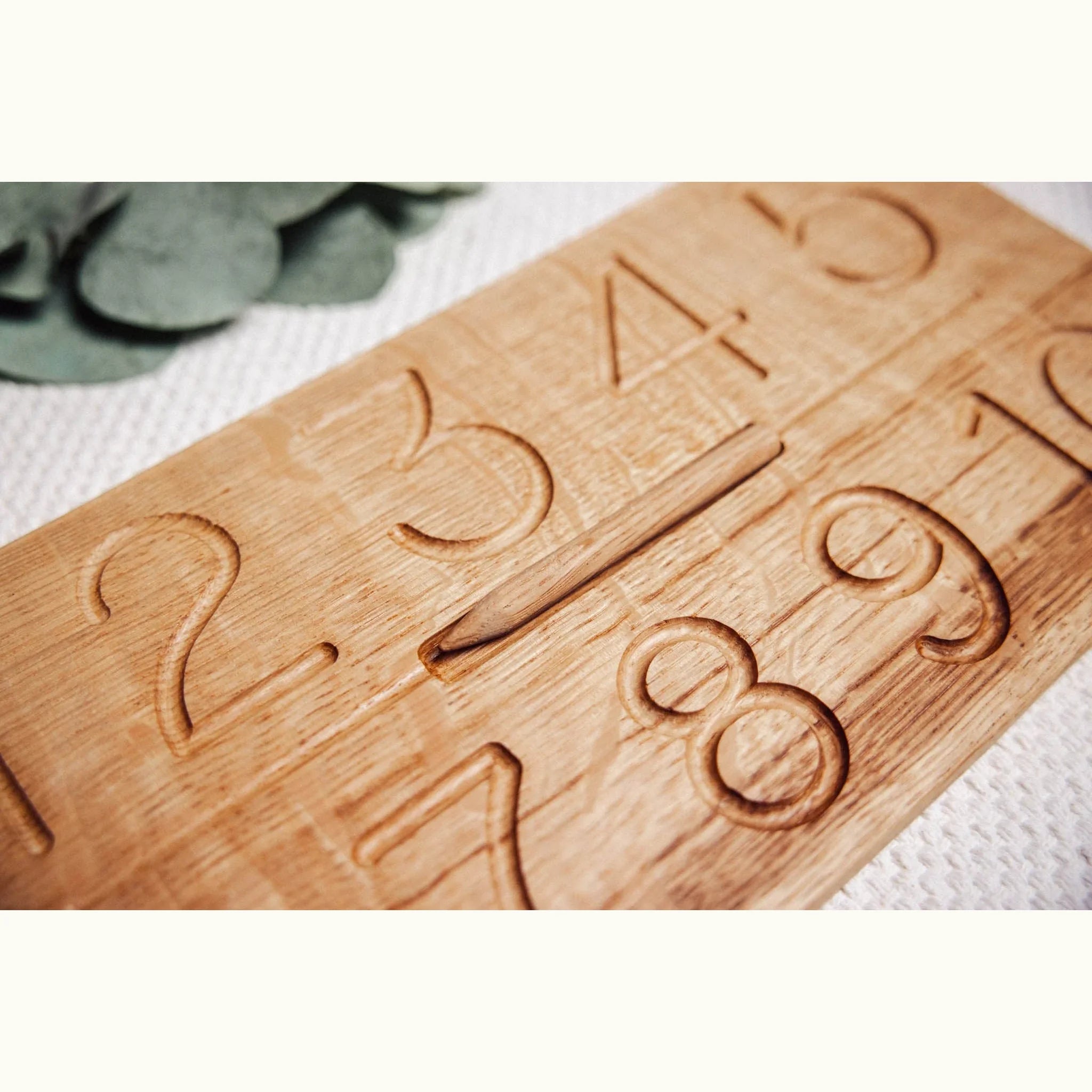 Close-up of Numbers Tracing & Balls oak board showing carved number channels with warm honey-tan grain and precise routed gro