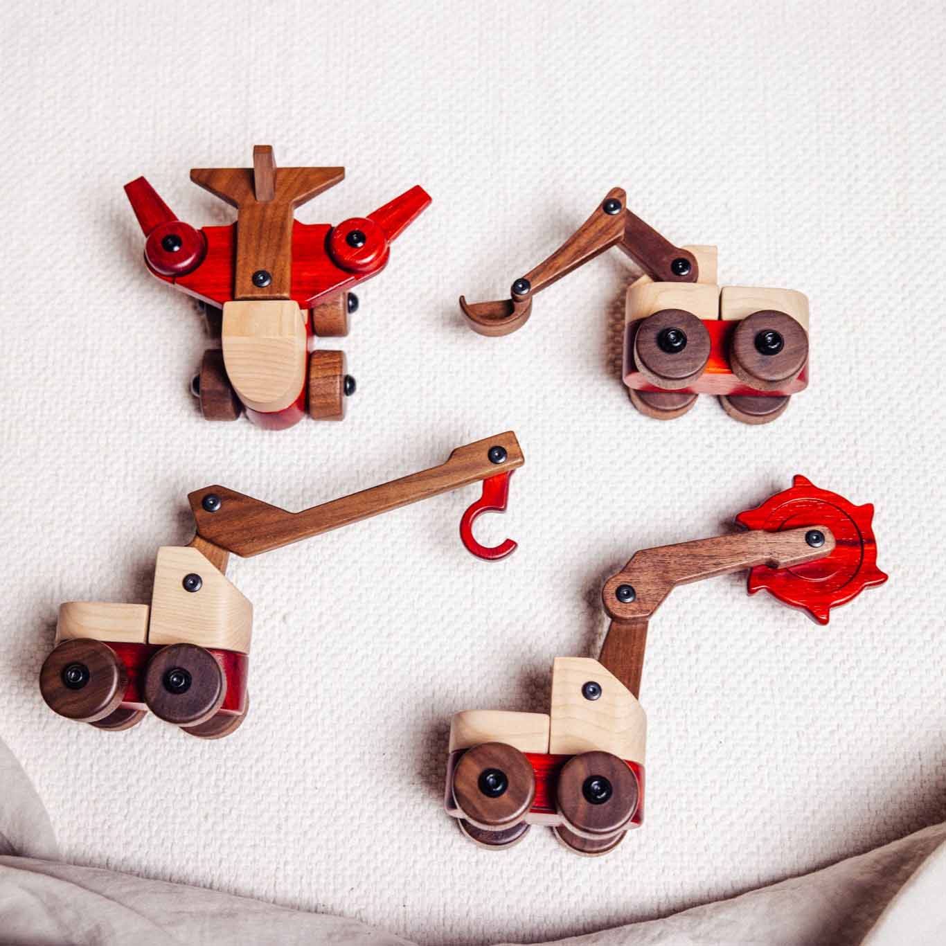 Padauk & Maple Trench Digger among four wooden construction vehicle toys on linen, showing maple, walnut and padauk tones