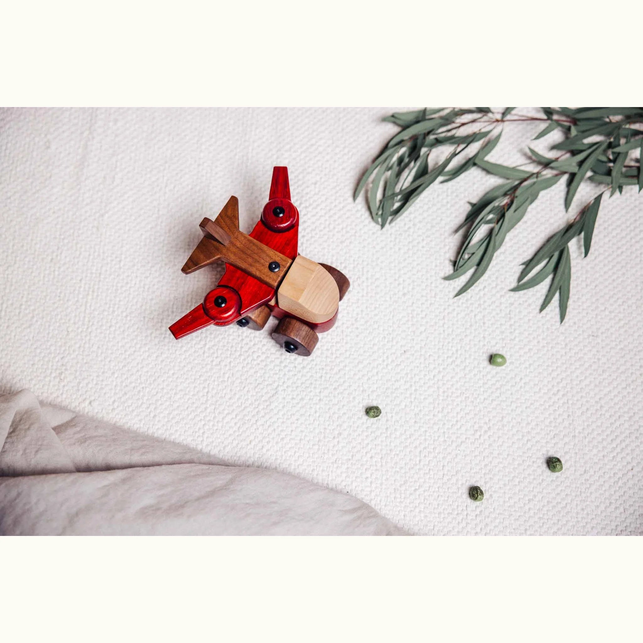 Walnut & Padauk Aeroplane flat-lay from above on linen, showing maple body, coral padauk wings, dark walnut tail