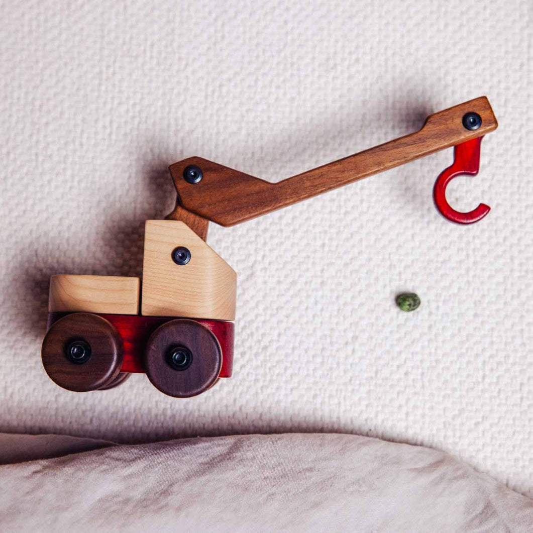 Wooden toy crane on a textured surface with a plant in the corner
