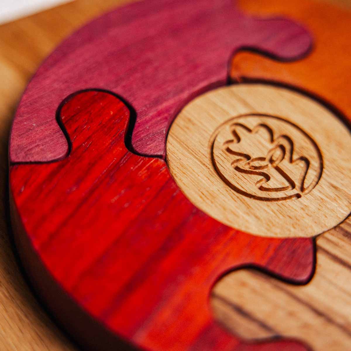 Unity Puzzle close-up: interlocking Padauk and Purpleheart curved segments beside laser-engraved Oak & Sprout branded oak dis