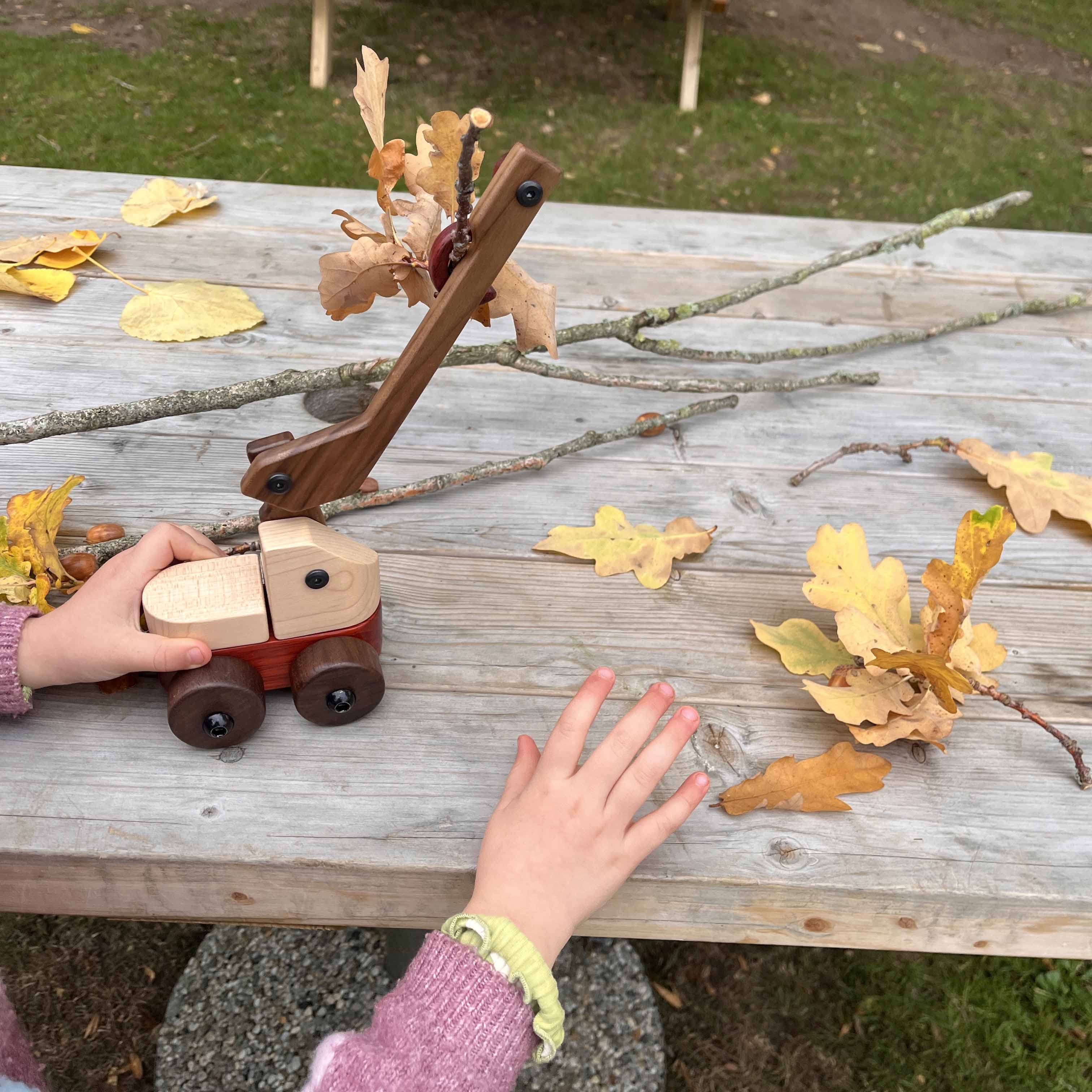 Child's hands playing with Walnut & Maple Crane outdoors, maple body, walnut boom and wheels, padauk base, autumn leaves near