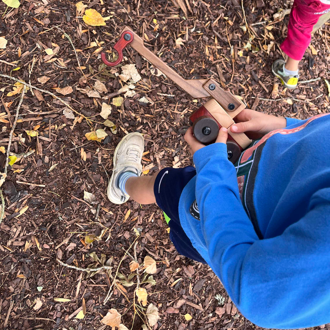 Child in blue hoodie playing with Walnut & Maple Crane outdoors, walnut boom and coral padauk hook accent visible
