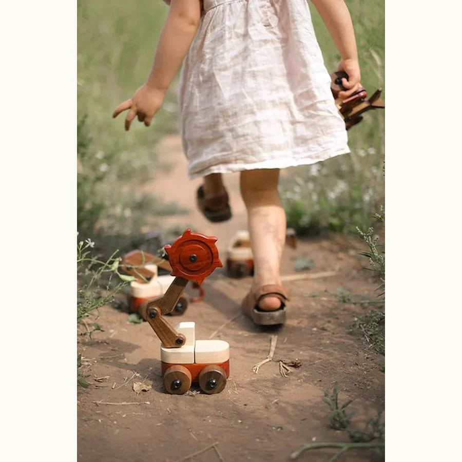 Padauk & Maple Trench Digger on a dirt path outdoors, coral-red padauk cutter wheel and pale maple body, child walking past