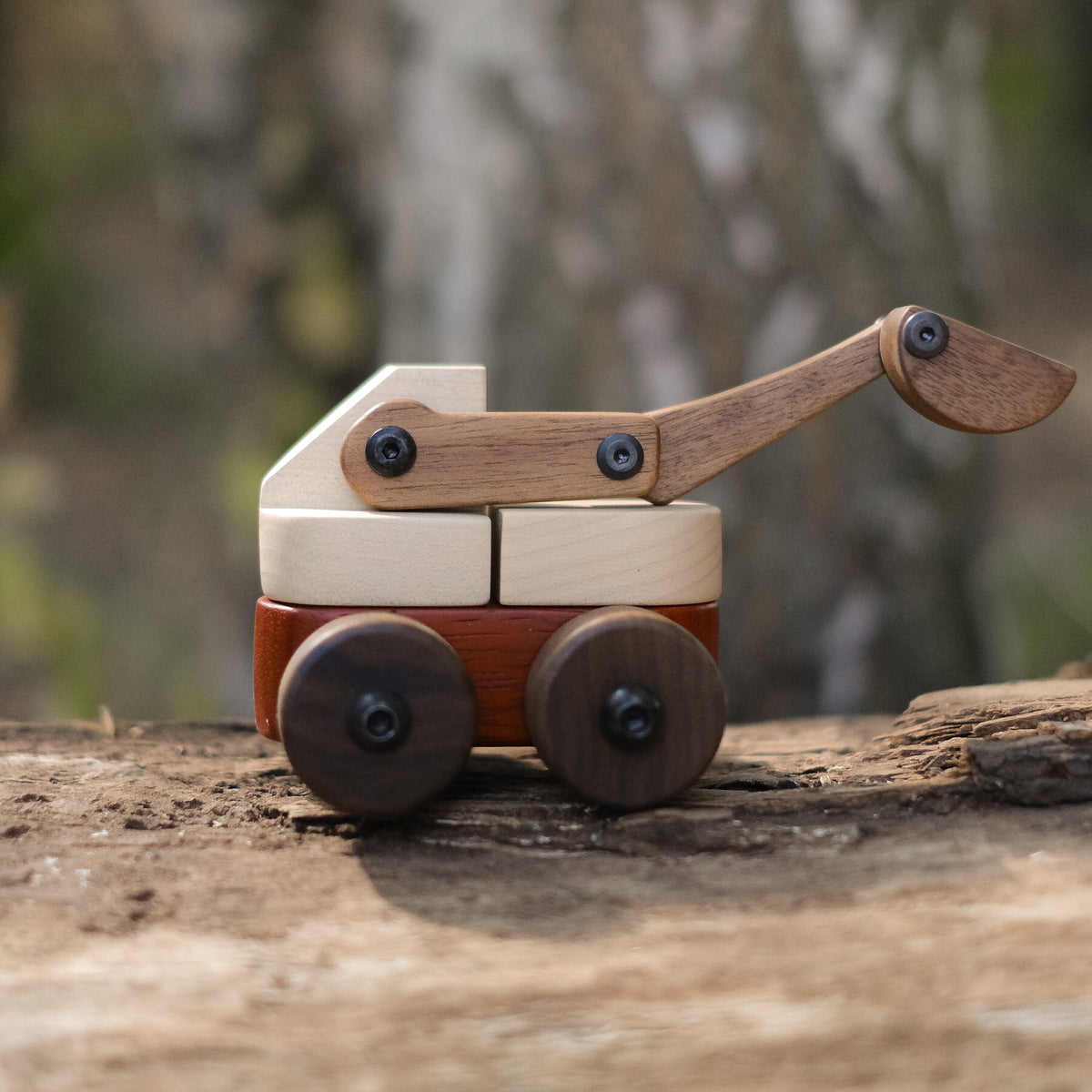 Maple & Padauk Excavator side view on a weathered log in the woods, maple body, padauk base, walnut arm, bucket and wheels