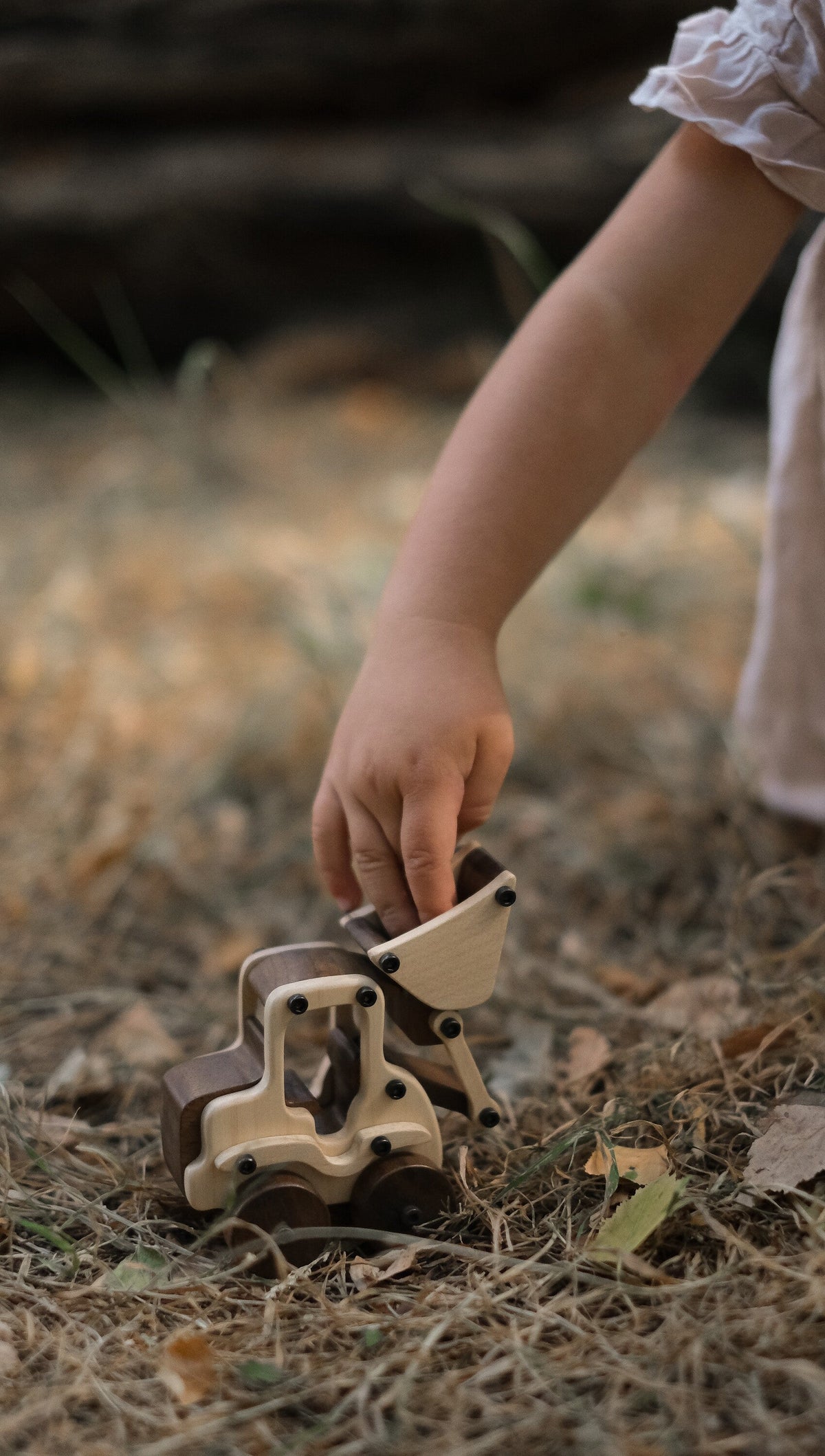Child reaching to play with Maple Digger outdoors on grass and earth, showing pale maple body and dark walnut wheels