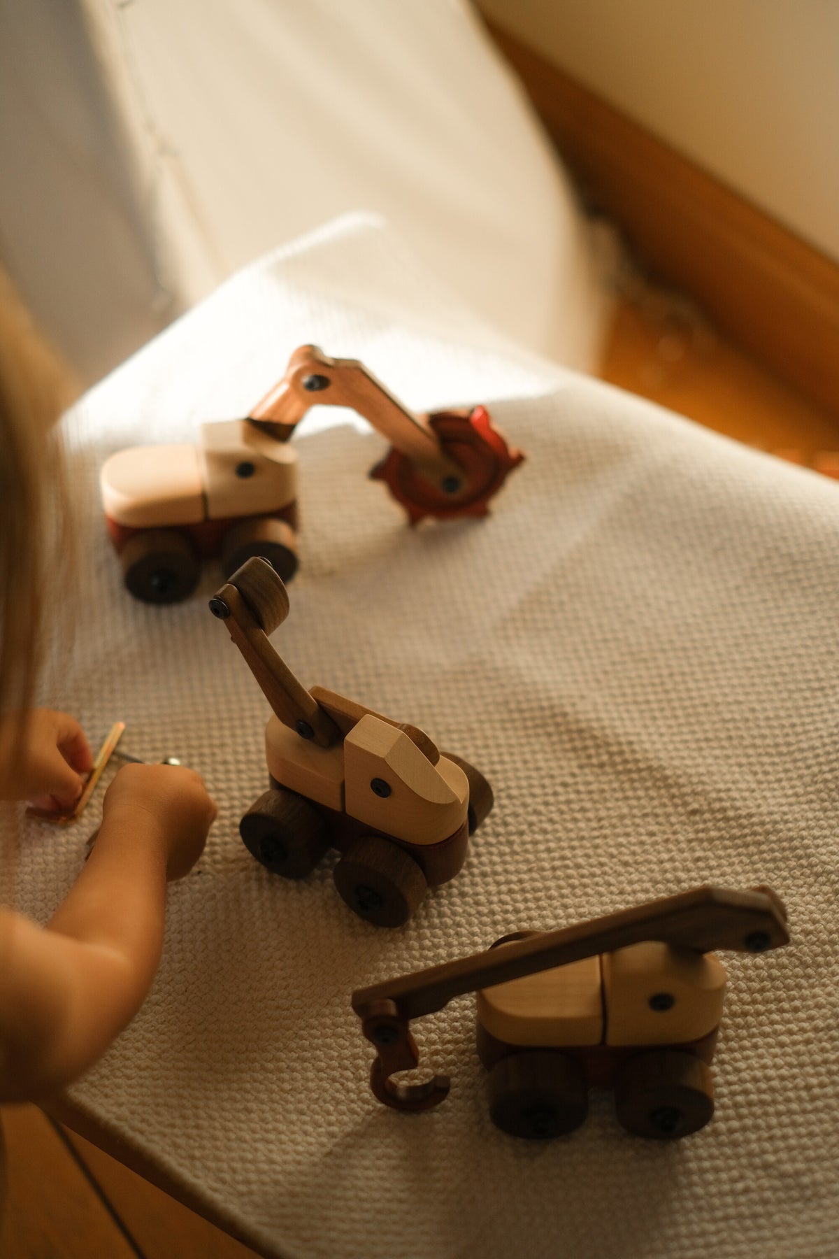 Child using an Allen key beside the crane, excavator and trench digger from the set on a white textured throw in sunlight