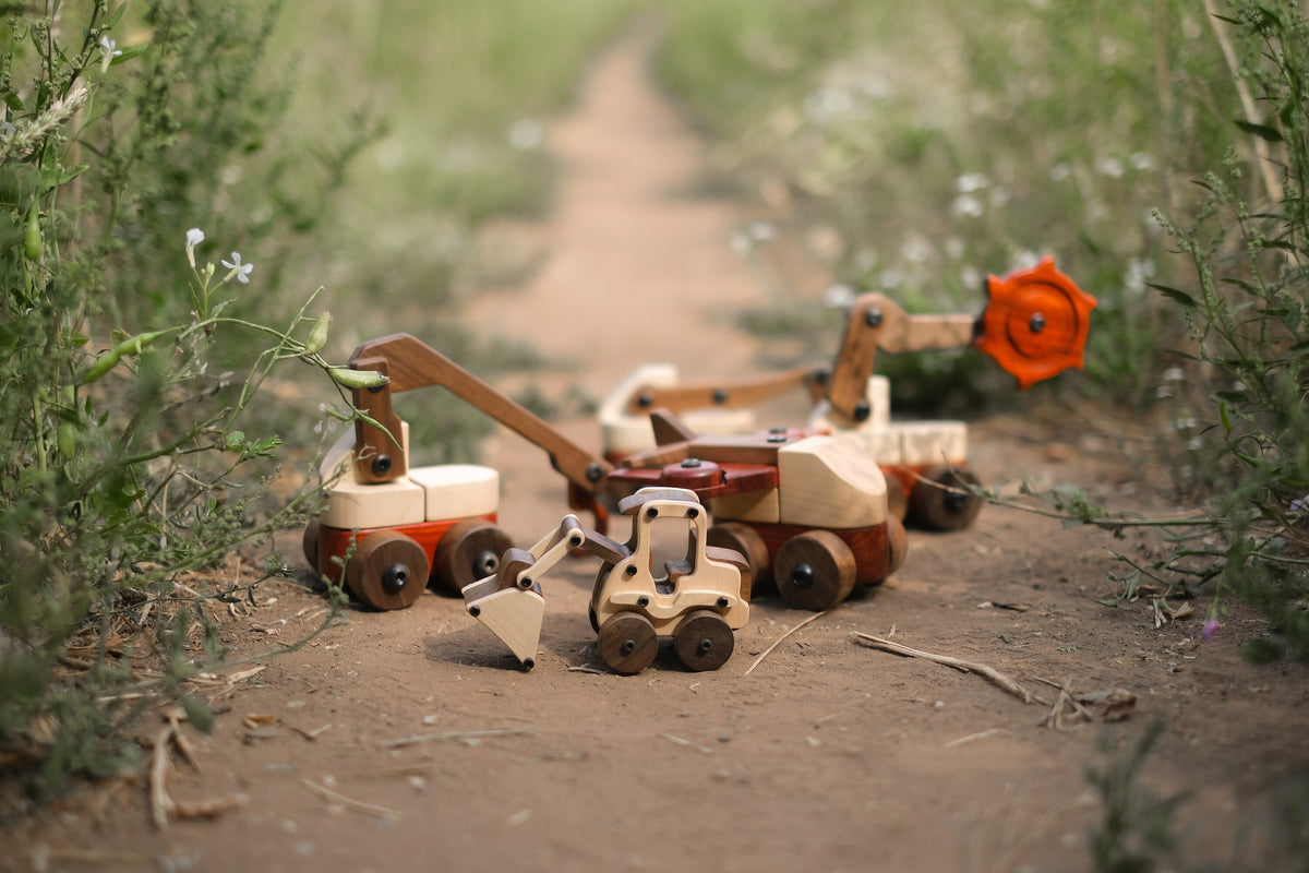 Maple Digger in pale maple and walnut displayed outdoors on a dirt path with wildflowers and wooden construction vehicle