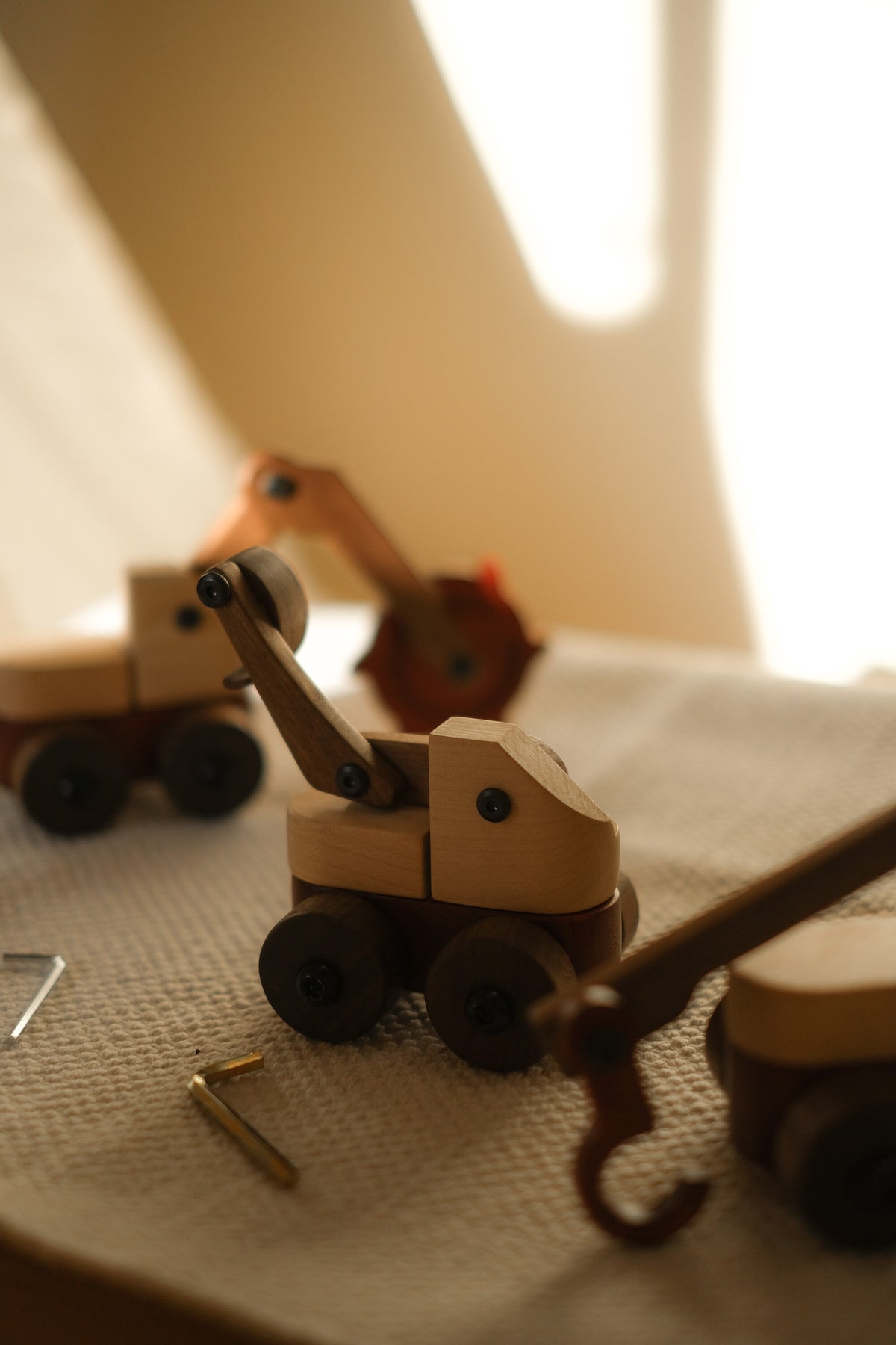 Padauk & Maple Trench Digger in soft focus behind the excavator and crane on a textured throw in warm window light, with Allen keys beside