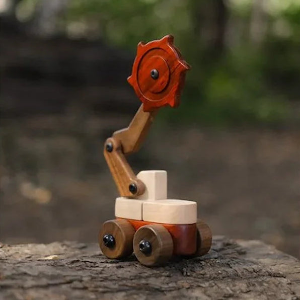 Padauk & Maple Trench Digger assembled on a log outdoors, showing padauk cutter wheel, maple chassis, and walnut arm