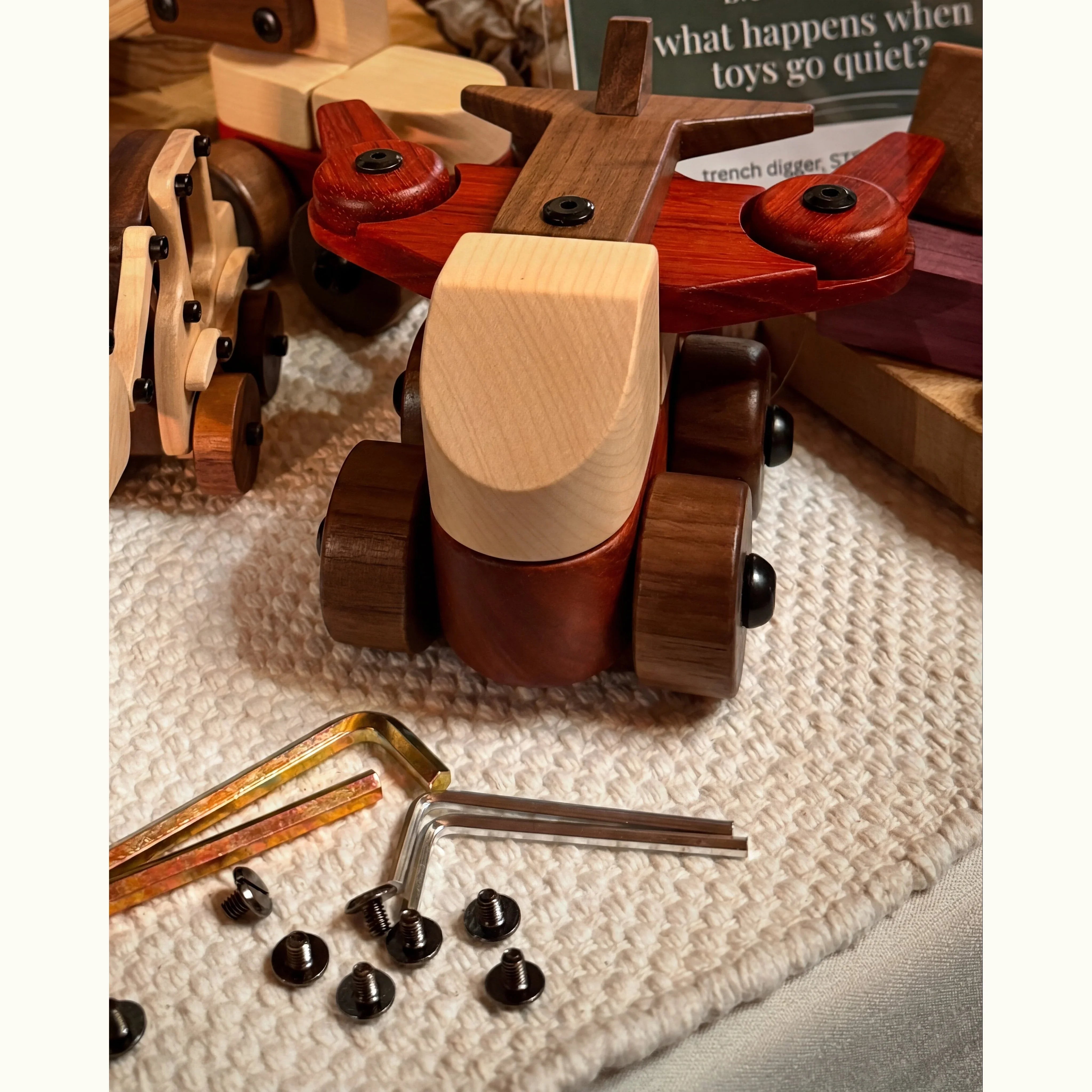 Walnut Padauk Maple aeroplane mid-disassembly with allen keys and screws on cream knit, showing tool-play mechanic