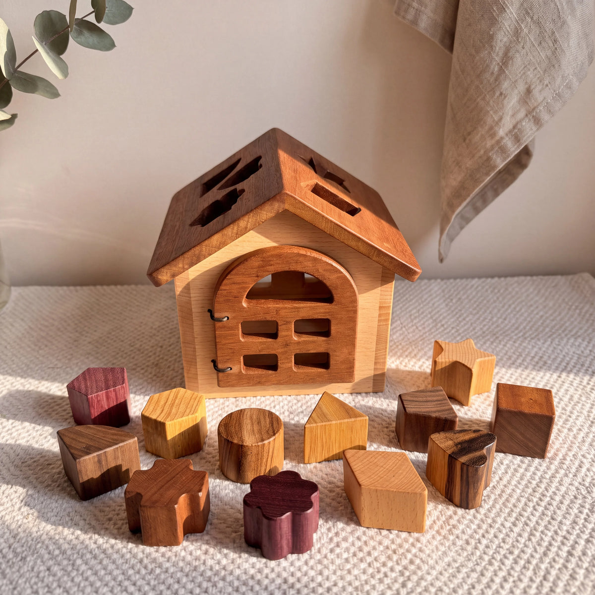 Shape Sorter House in beech and mahogany with all 12 hardwood blocks spread on cream knit playmat, showing purpleheart,