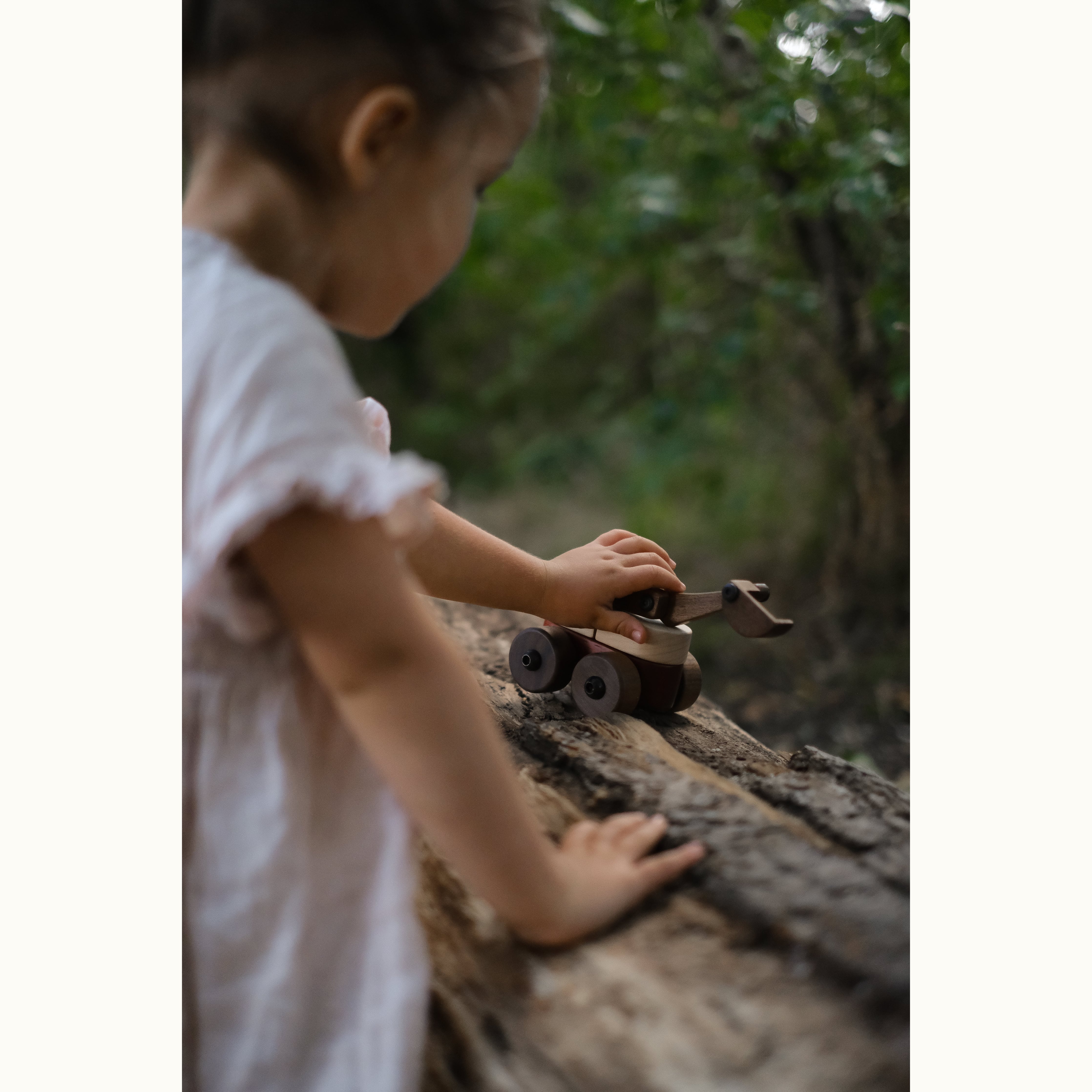 Toddler playing with Maple & Padauk Excavator on a fallen log outdoors, walnut body and maple mid-section visible