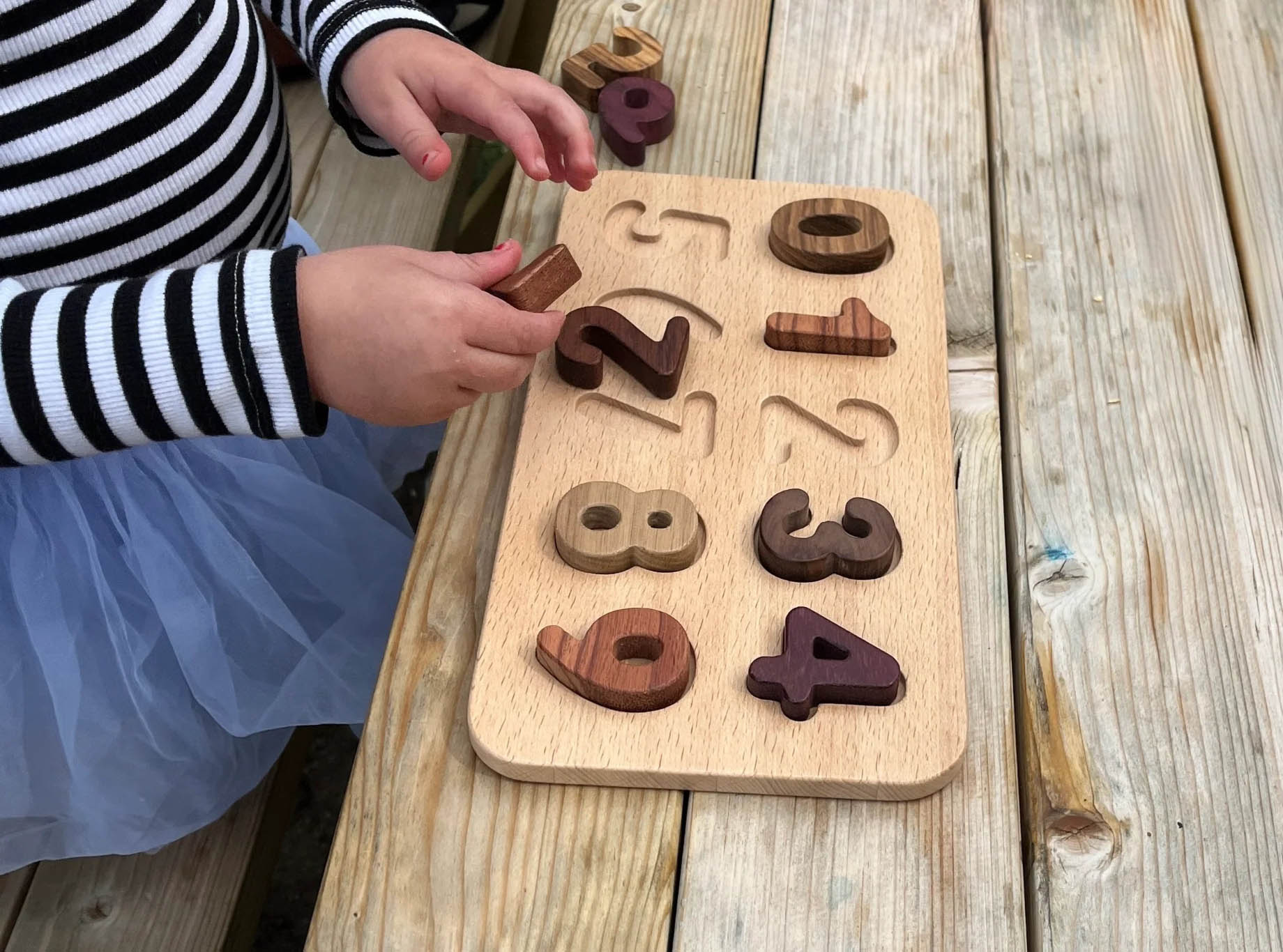 Child playing with a wooden number puzzle on a wooden surface