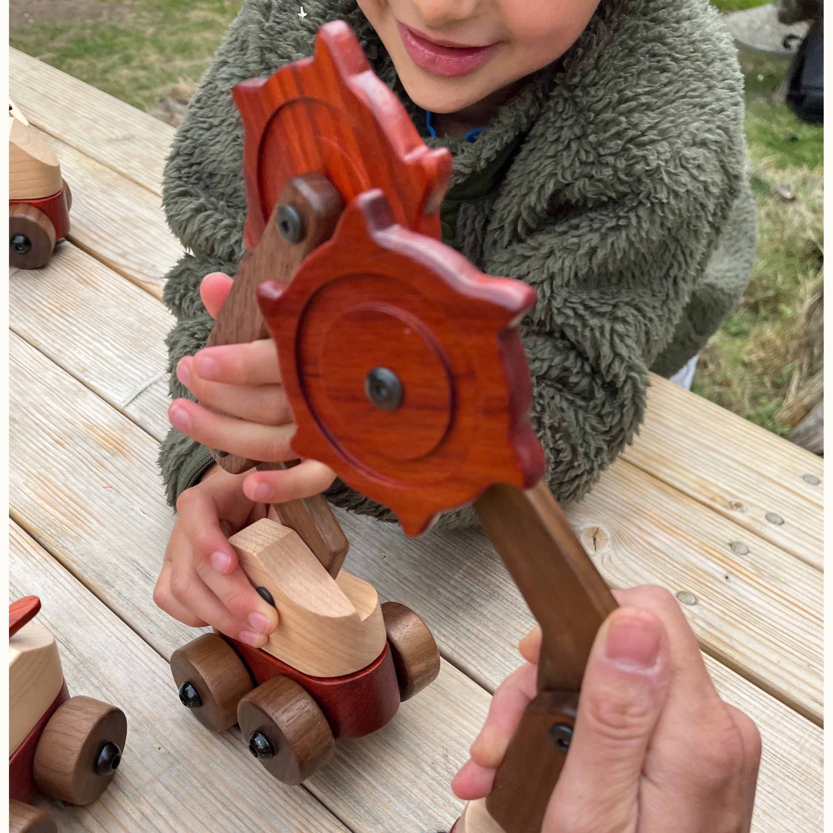 Child holding Padauk & Maple Trench Digger cutter wheel assembly outdoors, showing coral Padauk, dark Walnut, and cream Maple