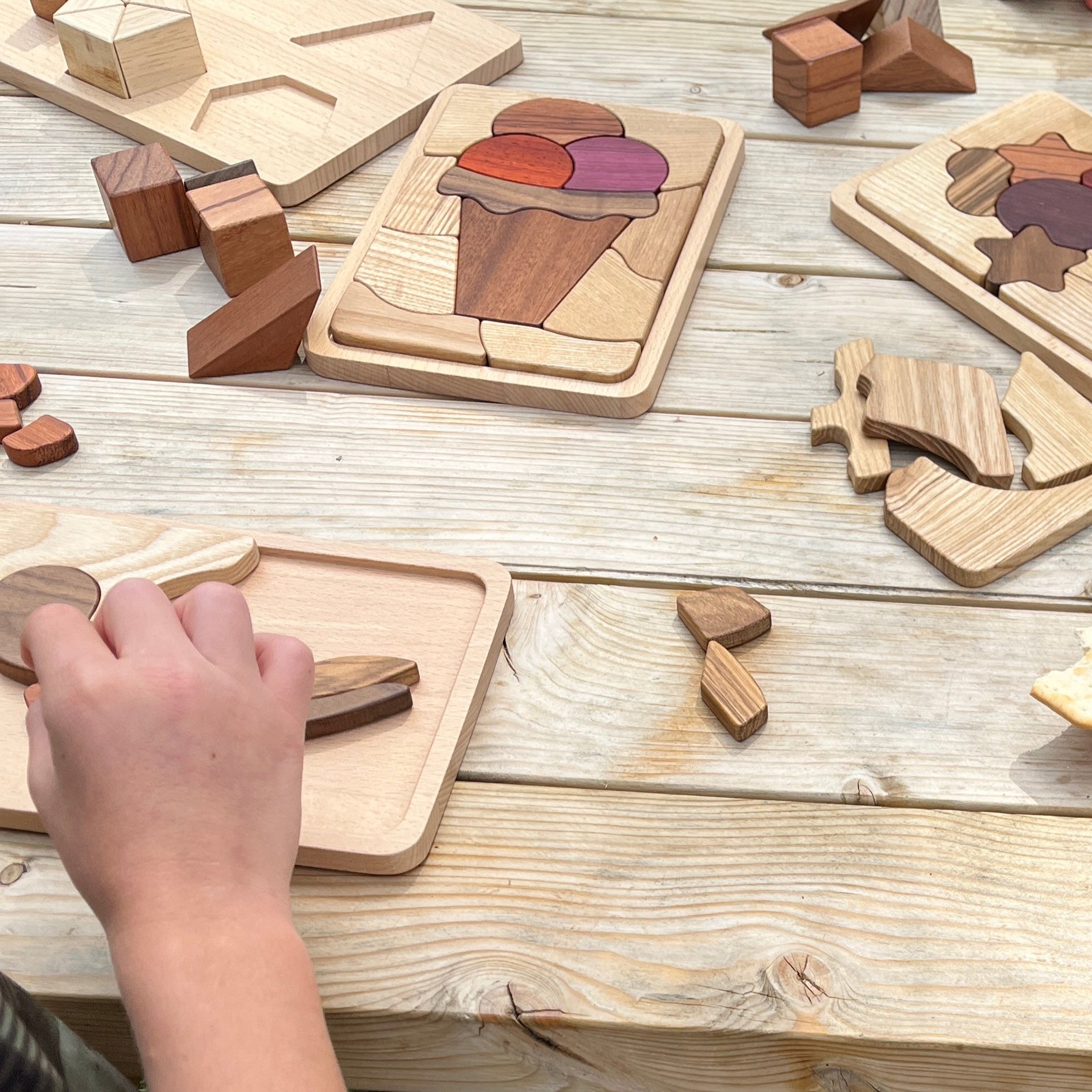 Children playing with wooden puzzle toys on a wooden table outdoors.