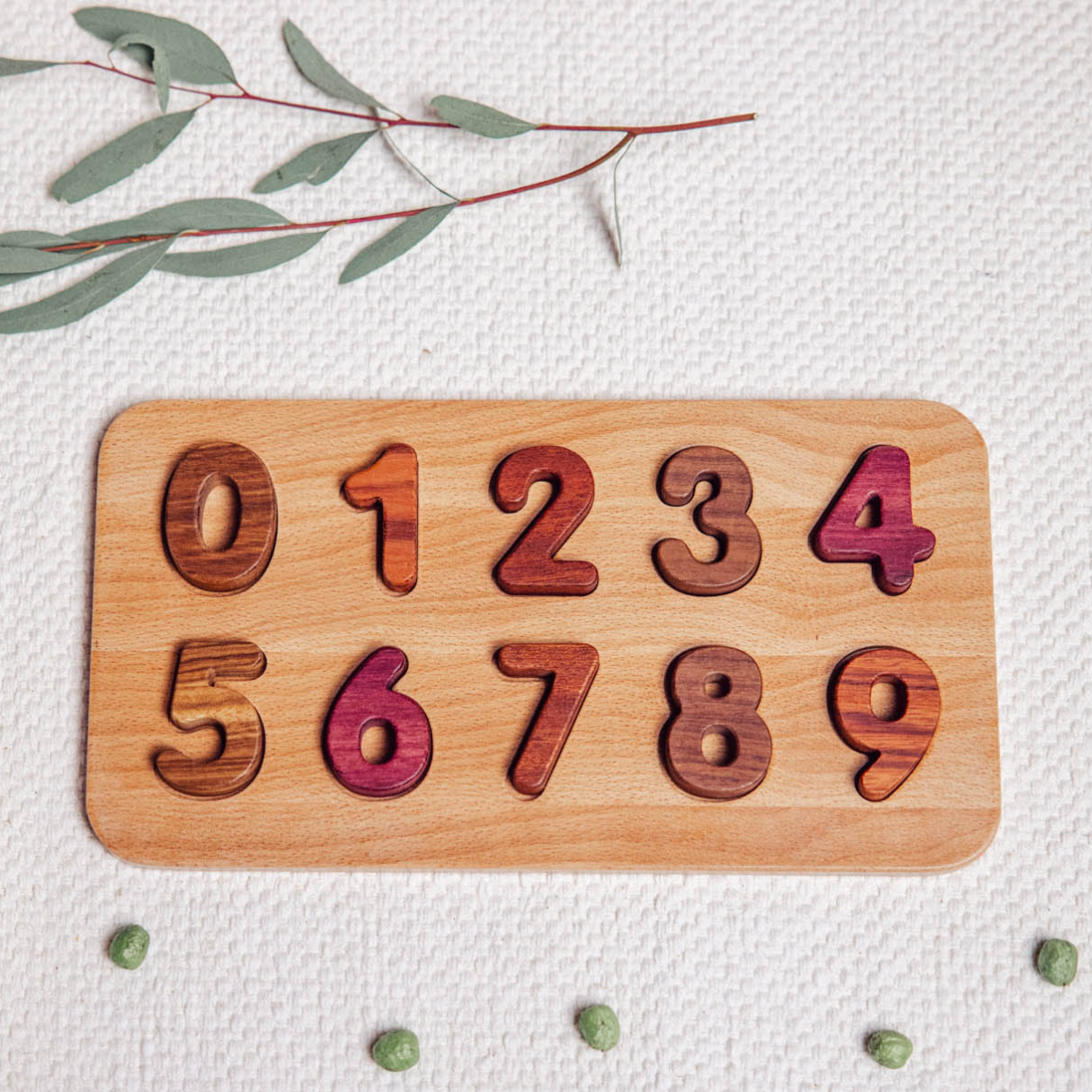 Wooden Number Puzzle 0–9 assembled flatlay showing Purpleheart, Walnut, Tigerwood and Mahogany pieces on linen
