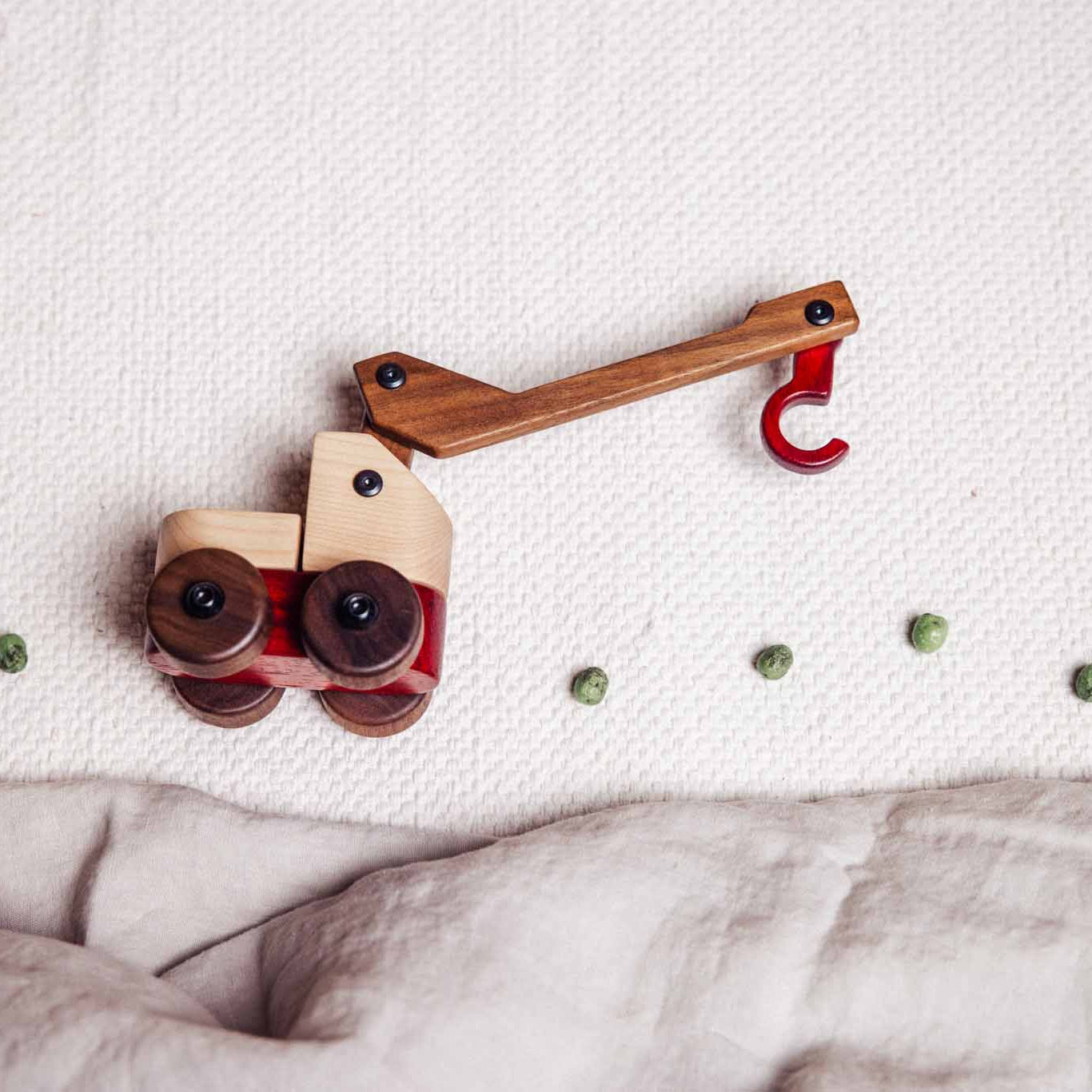 Walnut & Maple Crane toy, bird's-eye view: pale Maple cab, dark Walnut boom and wheels, coral Padauk hook extended