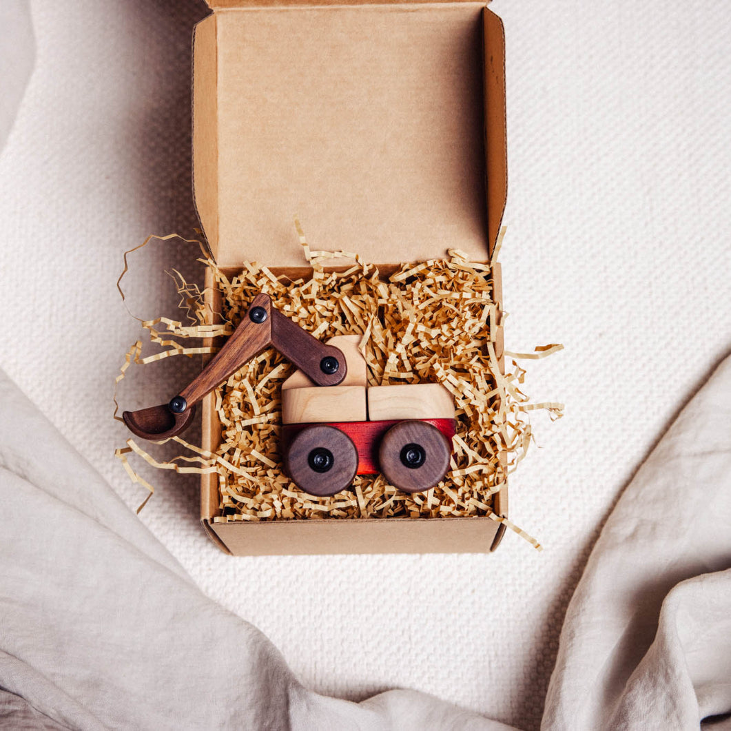 Wooden toy construction vehicle in a cardboard box on a soft fabric background