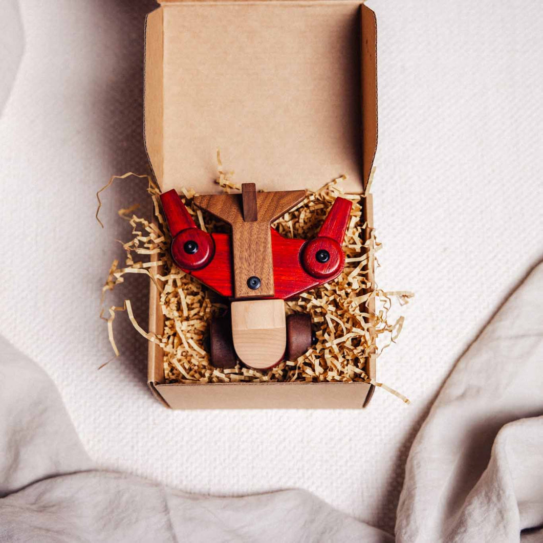 Wooden toy plane with red wings and brown body in a cardboard box on a light background