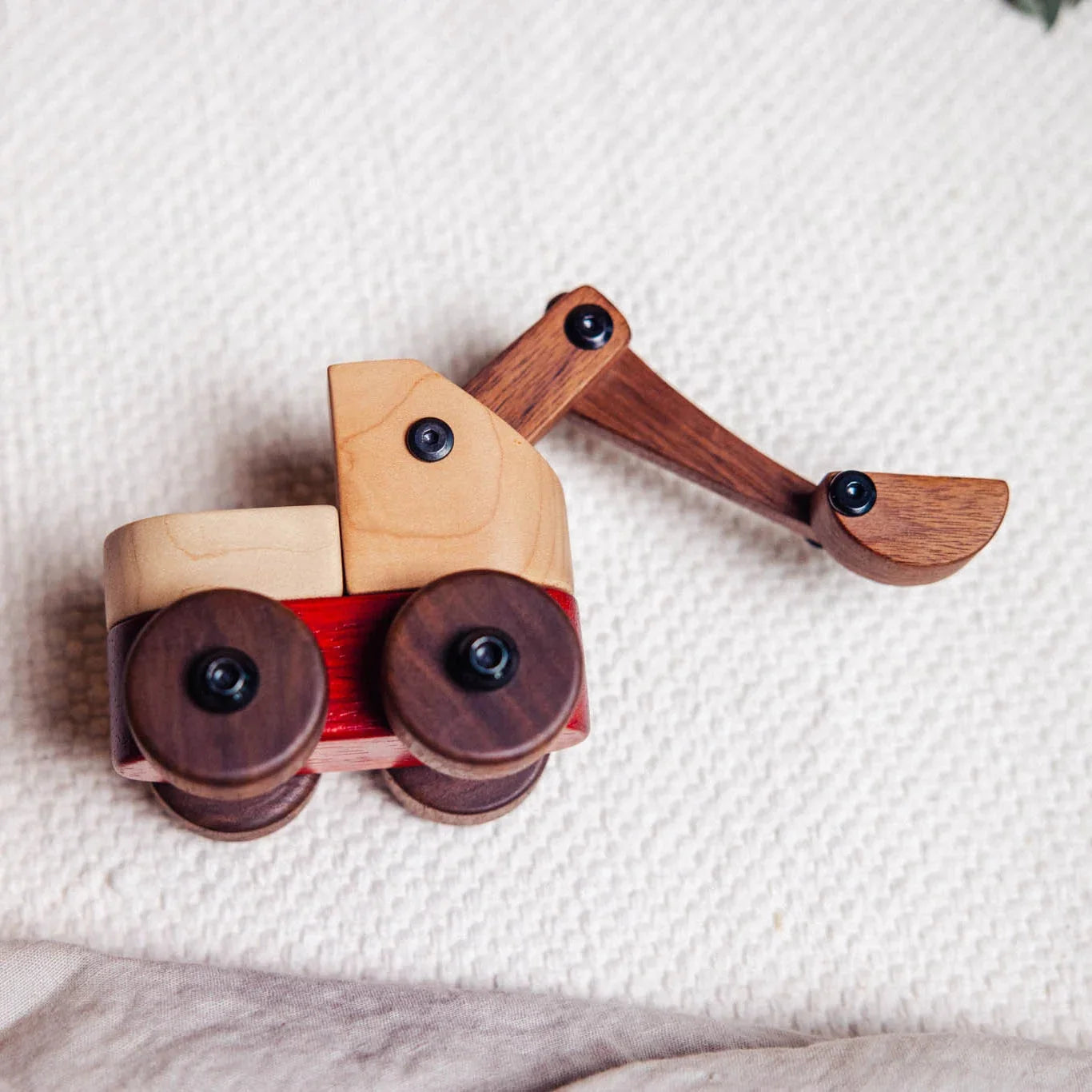 Maple Padauk Walnut Excavator toy overhead angle on cream knit surface, showing pale maple cab, coral padauk chassis stripe, 