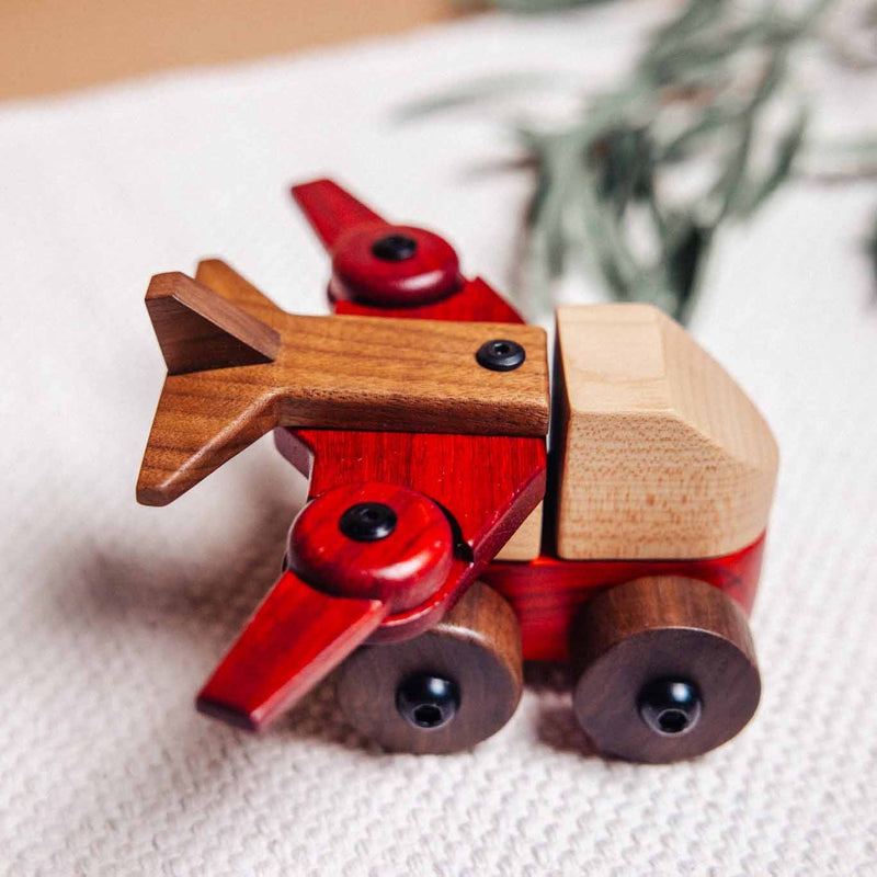 Walnut & Padauk Aeroplane close-up showing coral Padauk wings, dark Walnut wheels, and pale Maple cockpit on linen