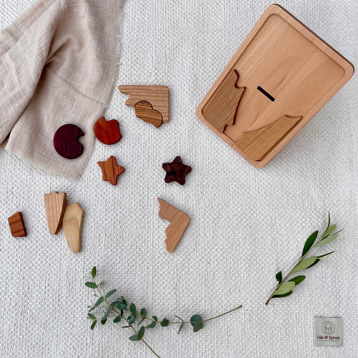 Beech shape-sorter with naturally coloured wood pieces (Padauk, Purpleheart, Zebrano) on white cotton play mat – Oak & Sprout